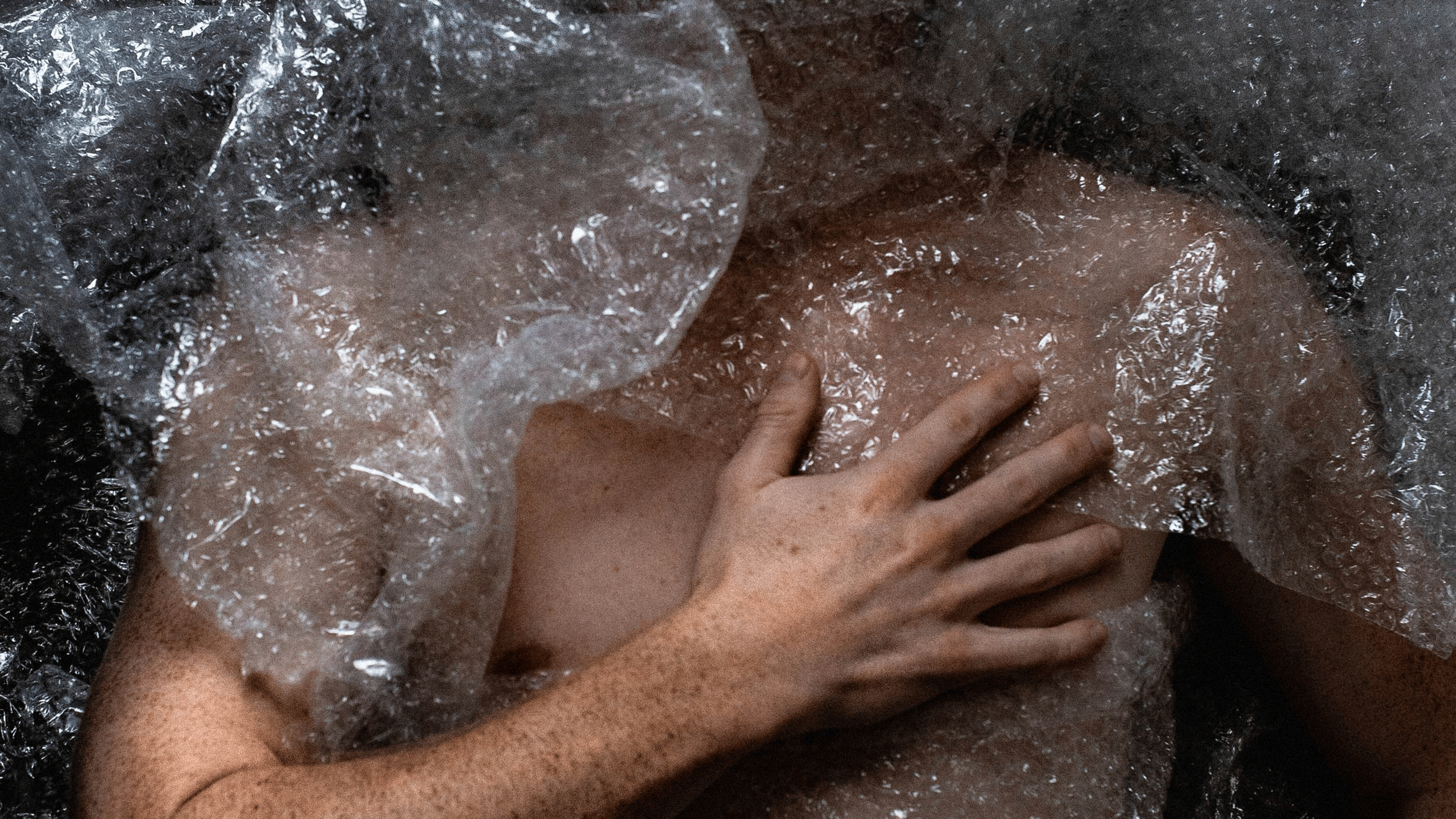 Person in Knisterfolie eigewickelt, Closed Up, greift sich an die Brust