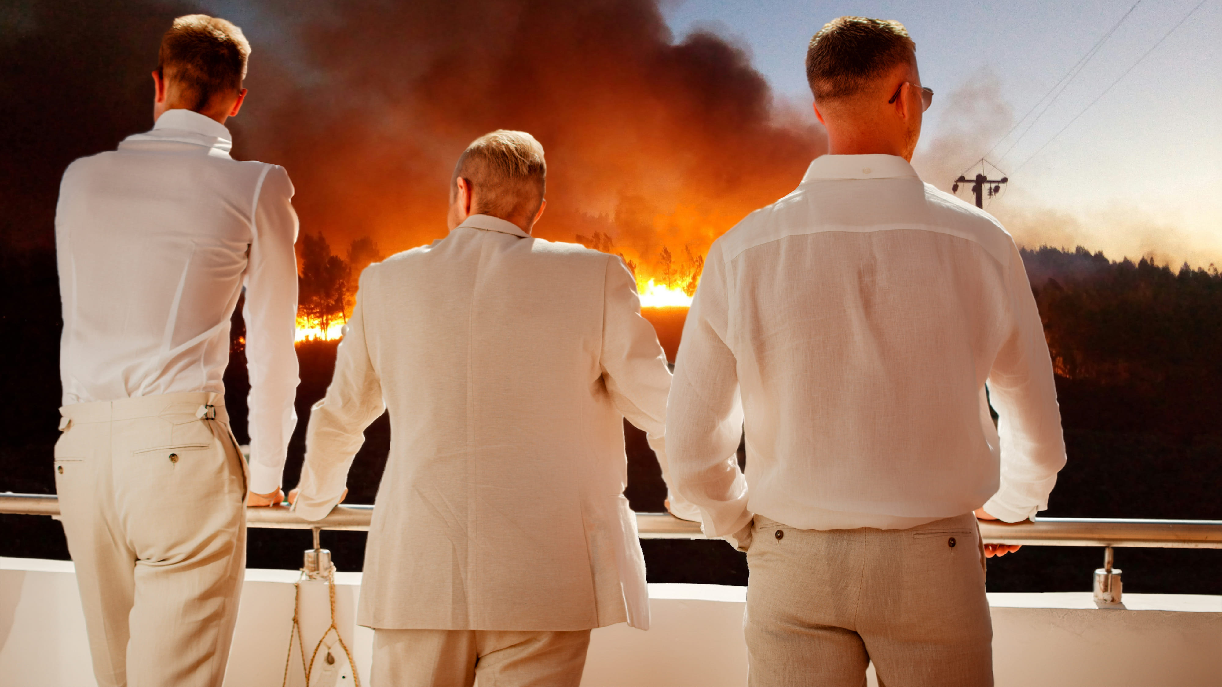 Drei Männer in weißen Hemden schauen, von einem Balkon zu, wie die Landschaft vor ihnen brennt. 