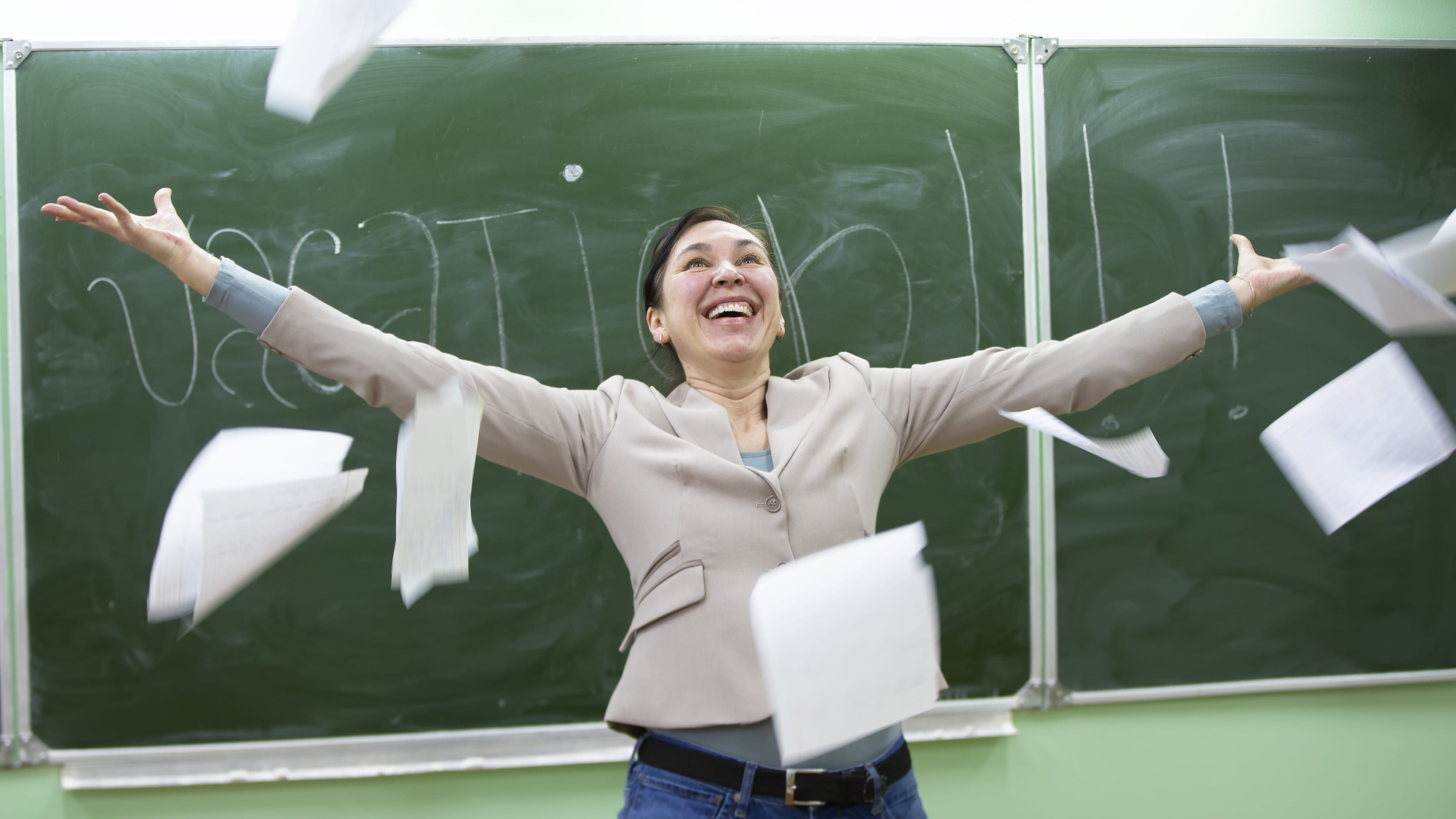 Eine jubelnde Frau vor einer grünen Tafel, auf der Vacation steht