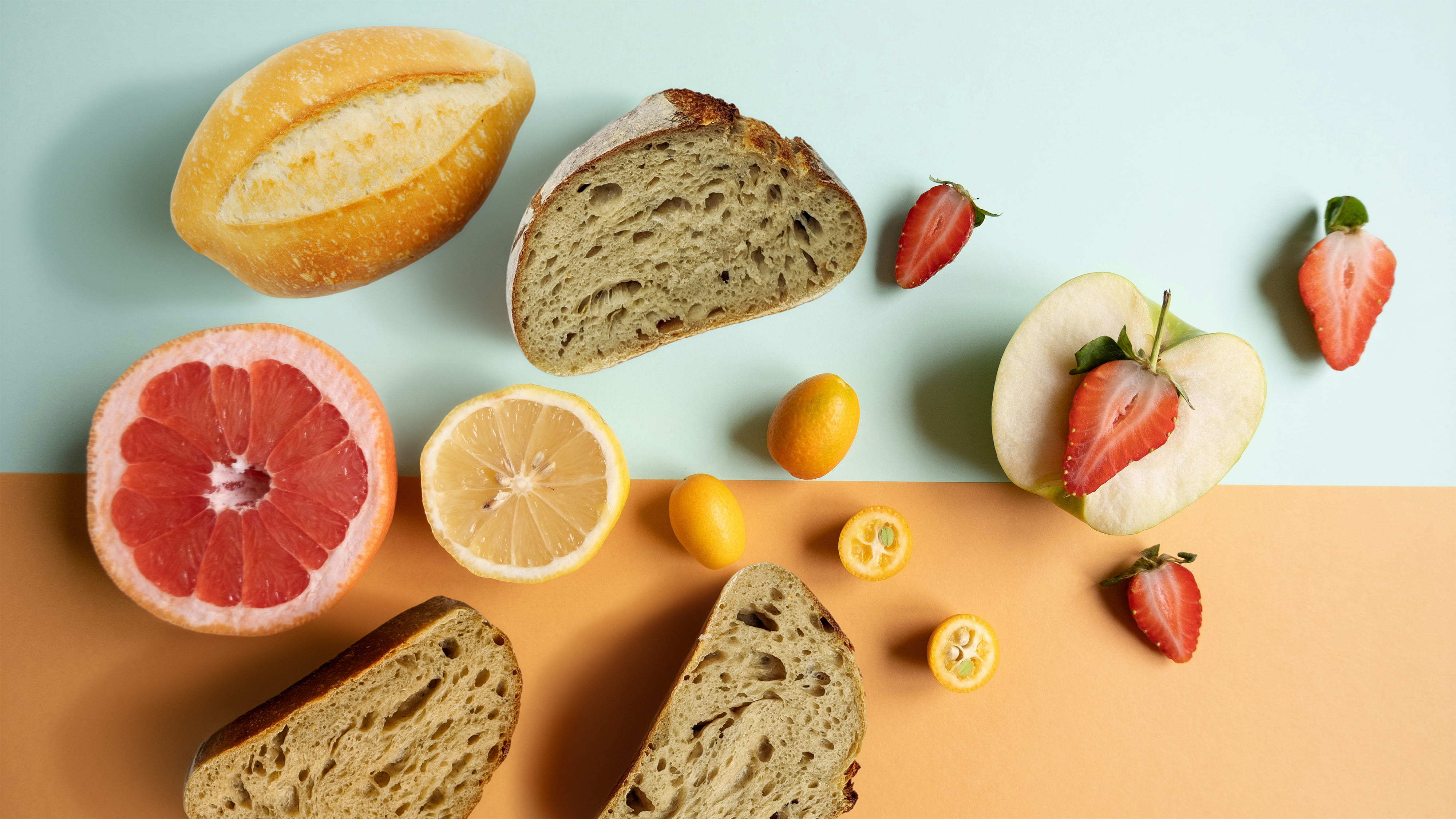 Aufgeschnittenes Brot, Früchte und Obst. Draufsicht vor farbigem Hintergrund.