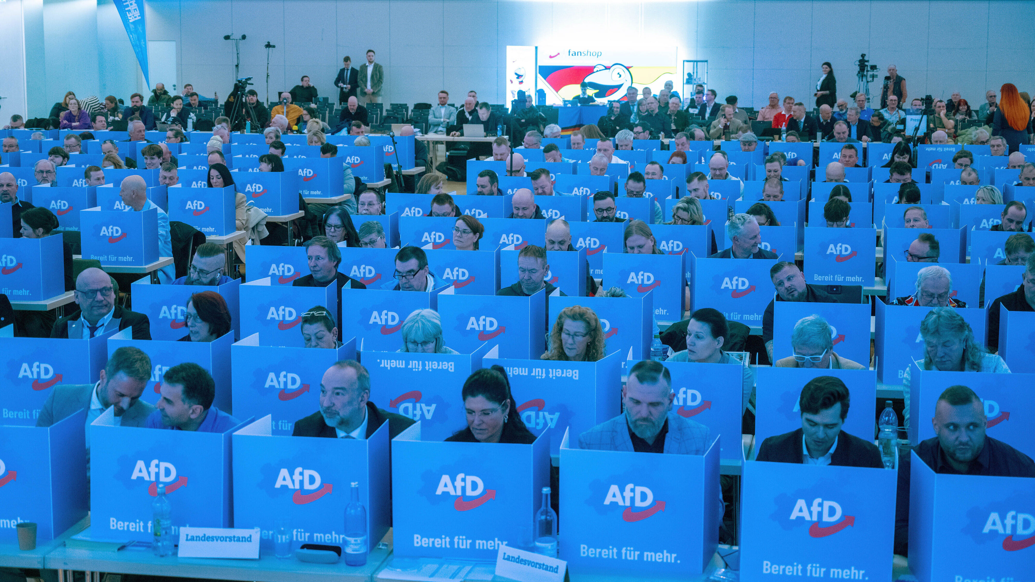 Mitglieder der AfD sitzen auf dem Listenparteitag hinter den persönlichen Wahlkabinen. 
