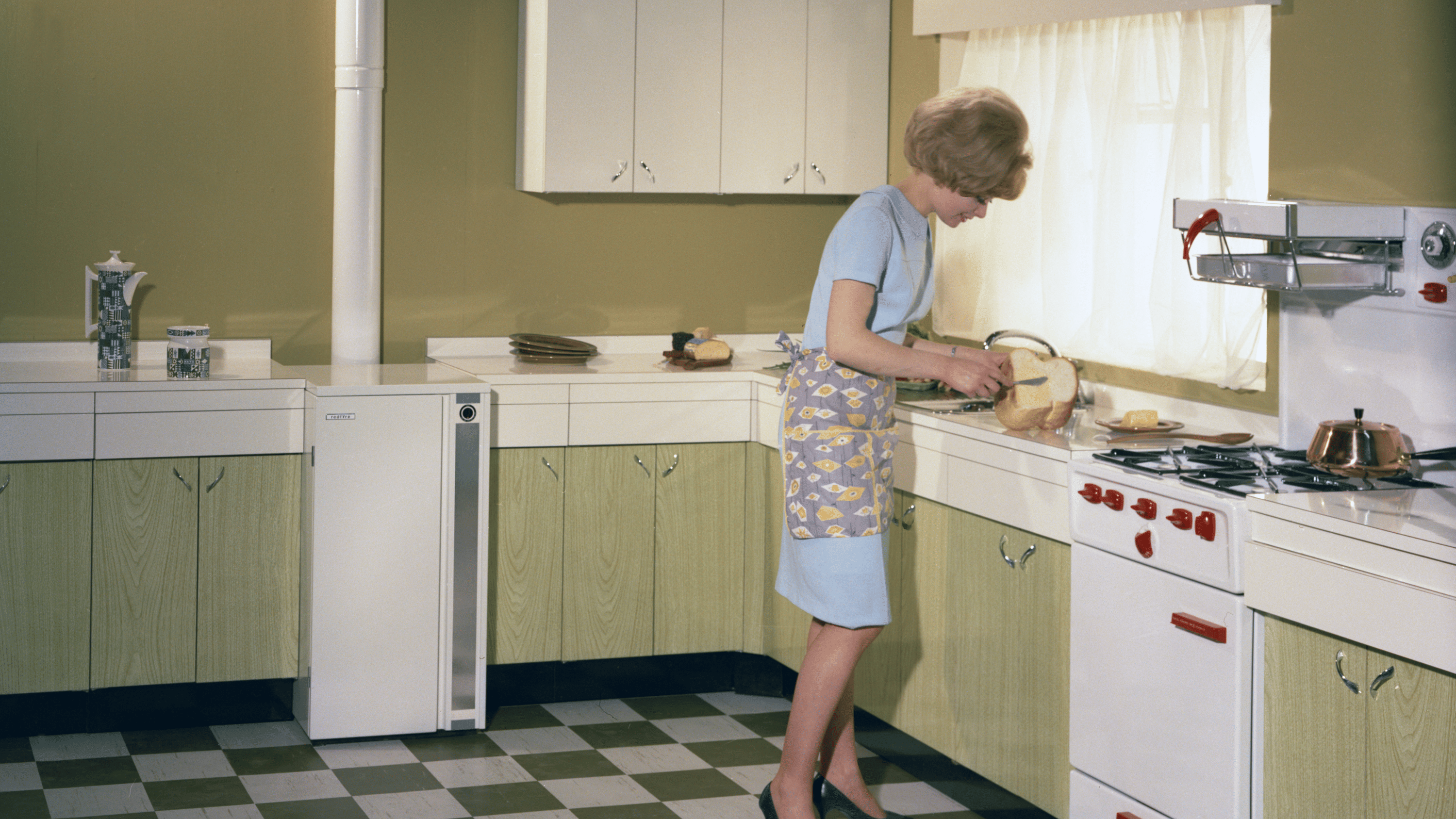 Eine Frau steht in einer altmodisch wirkenden Küche und schneidet Brot