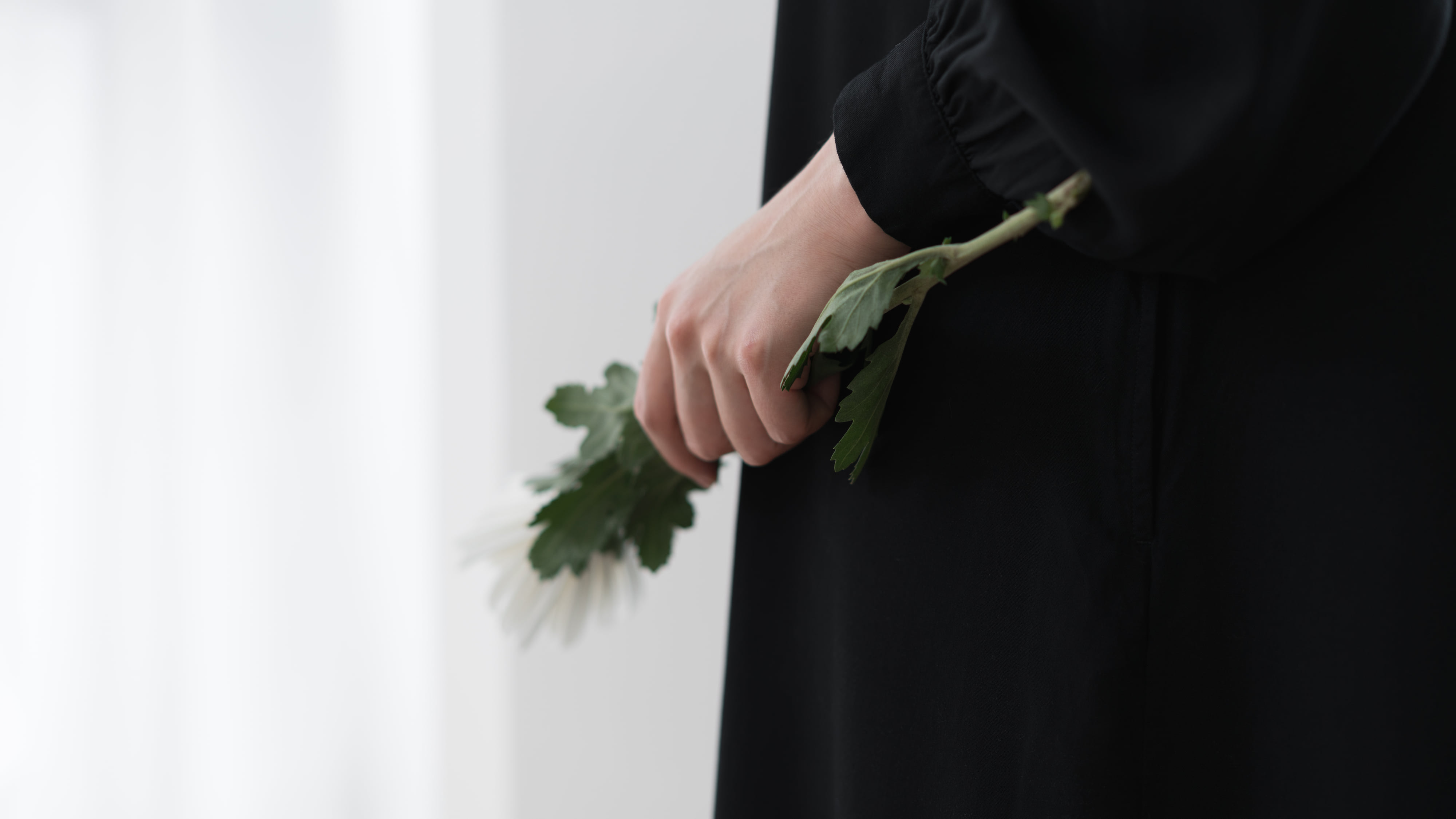 Eine Frau steht bei einer Beerdigung mit einer weißen Blume in der Hand.