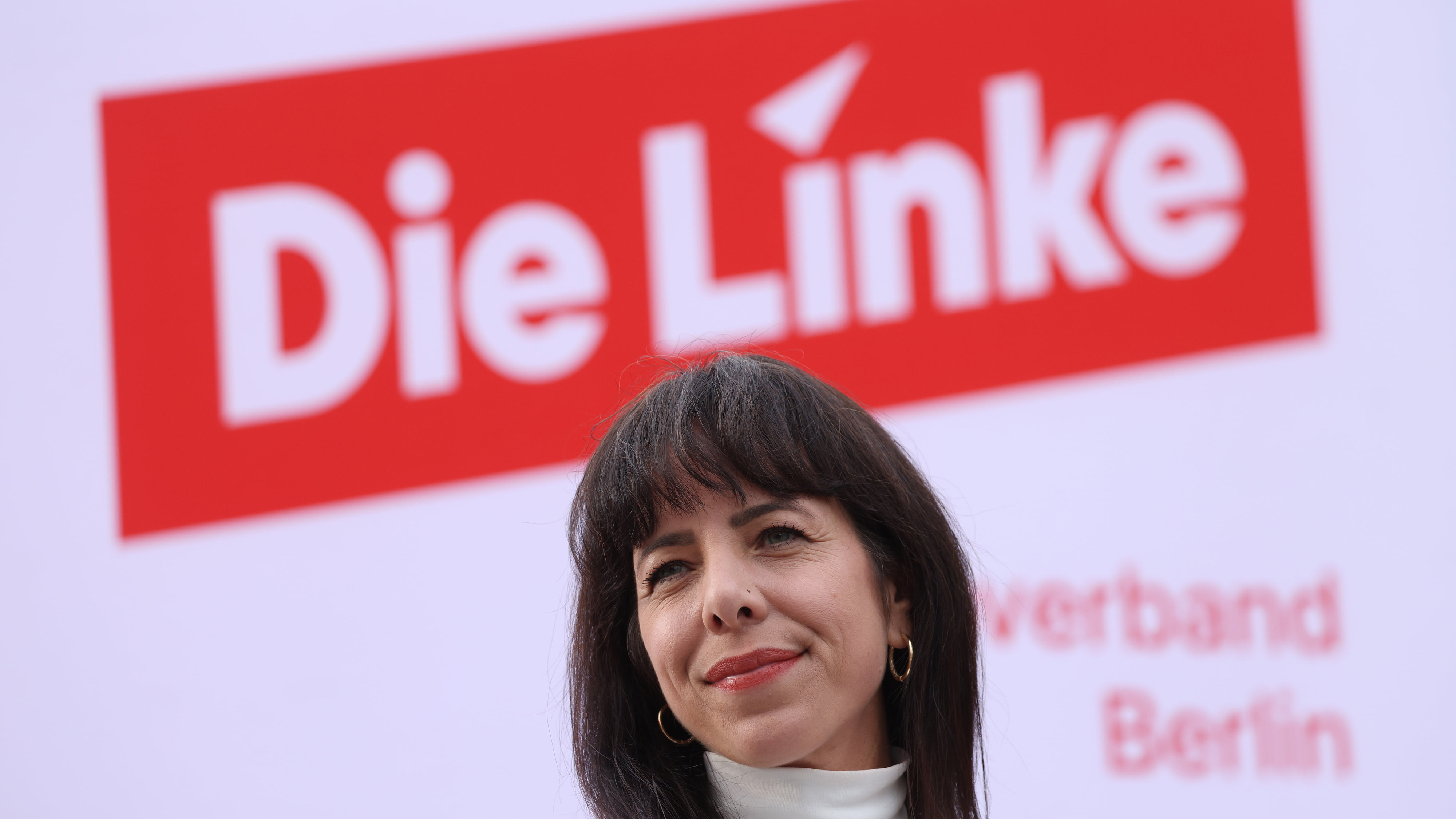 Die Linkenpolitikerin Elif Eralp lächelt vor einem Plakat der Partei.