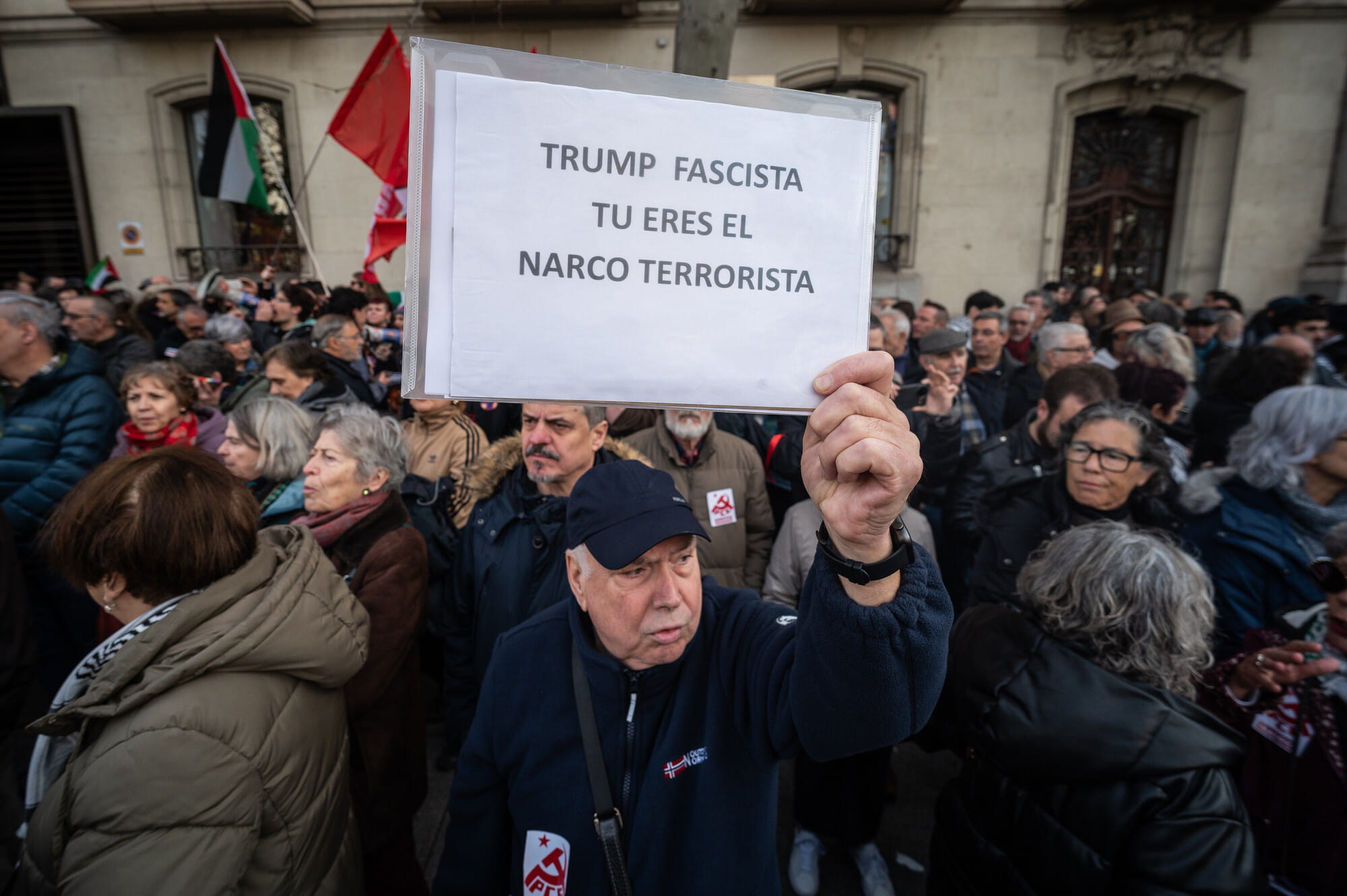 Man sieht einen Mann in einer Menge, der ein Schild hält, auf dem steht: Trump Fascista Tu Eres El Narco Terrorista