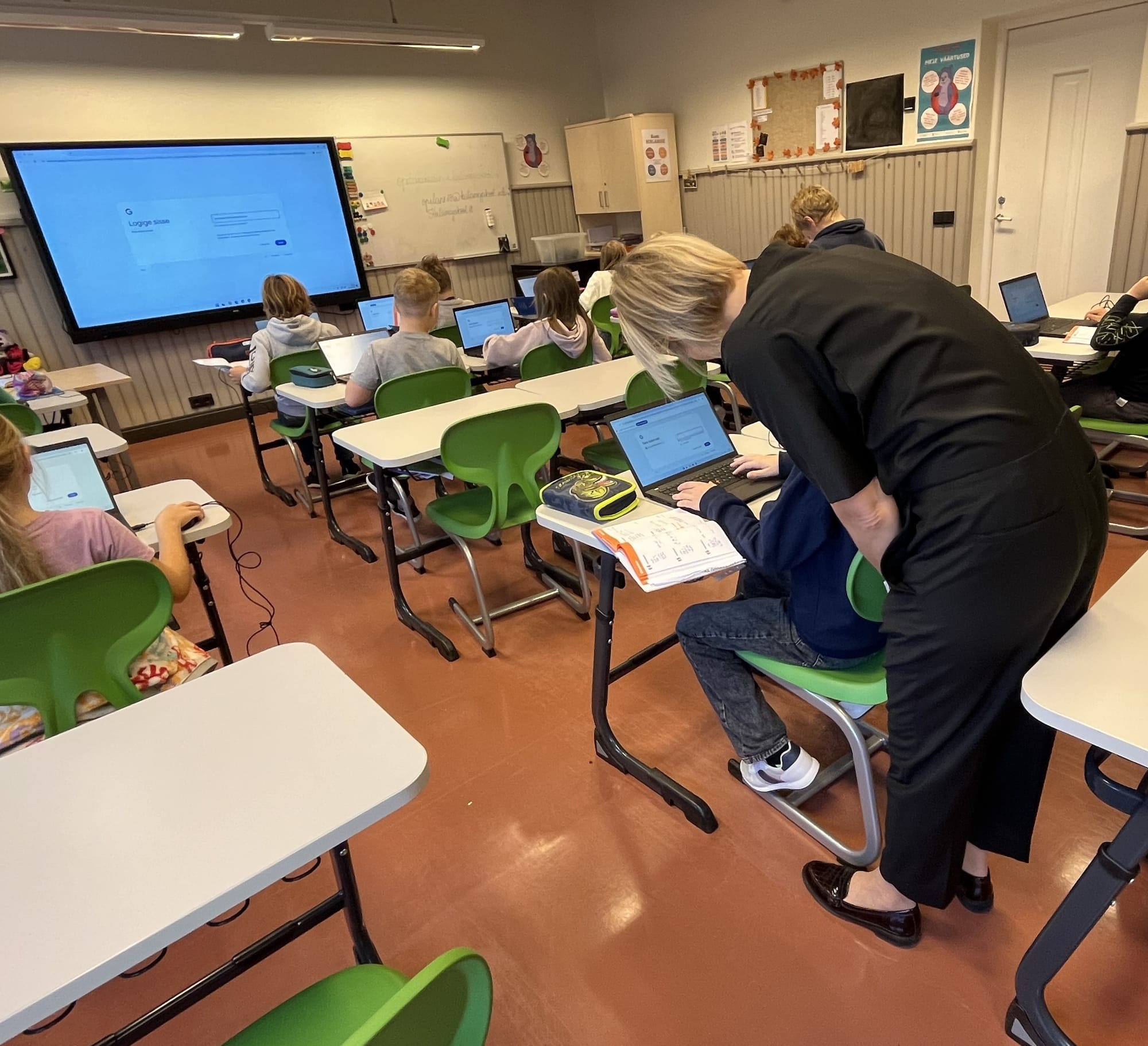 Eine Lehrerin hilft einem Schüler beim Einloggen in sein Google-Konto. Heute sollen die Kinder ihre erste eigene Mail verschicken. Dafür muss die Lehrerin auch erklären, wie eine Mail aufgebaut ist.