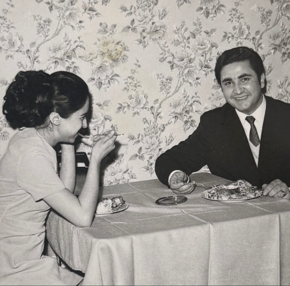 Ein Schwarz-Weiß-Foto von einer Frau und einem Mann, die an einem Tisch sitzen, essen und dabei lachen.