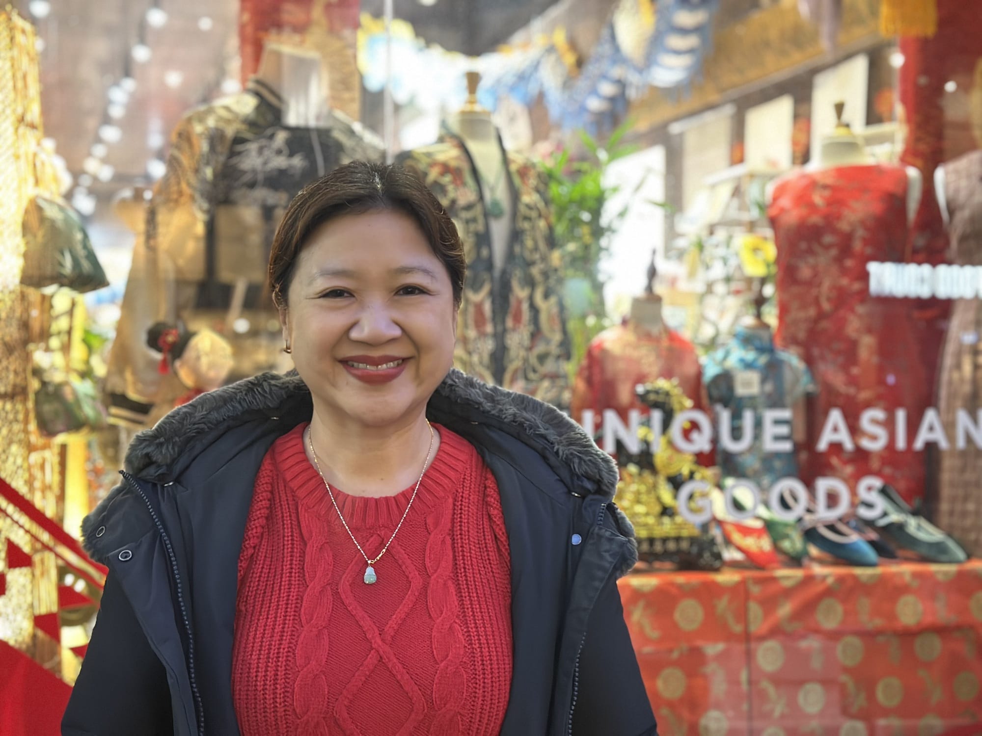 Man sieht eine Frau im roten Pullover vor einem bunten Schaufenster.
