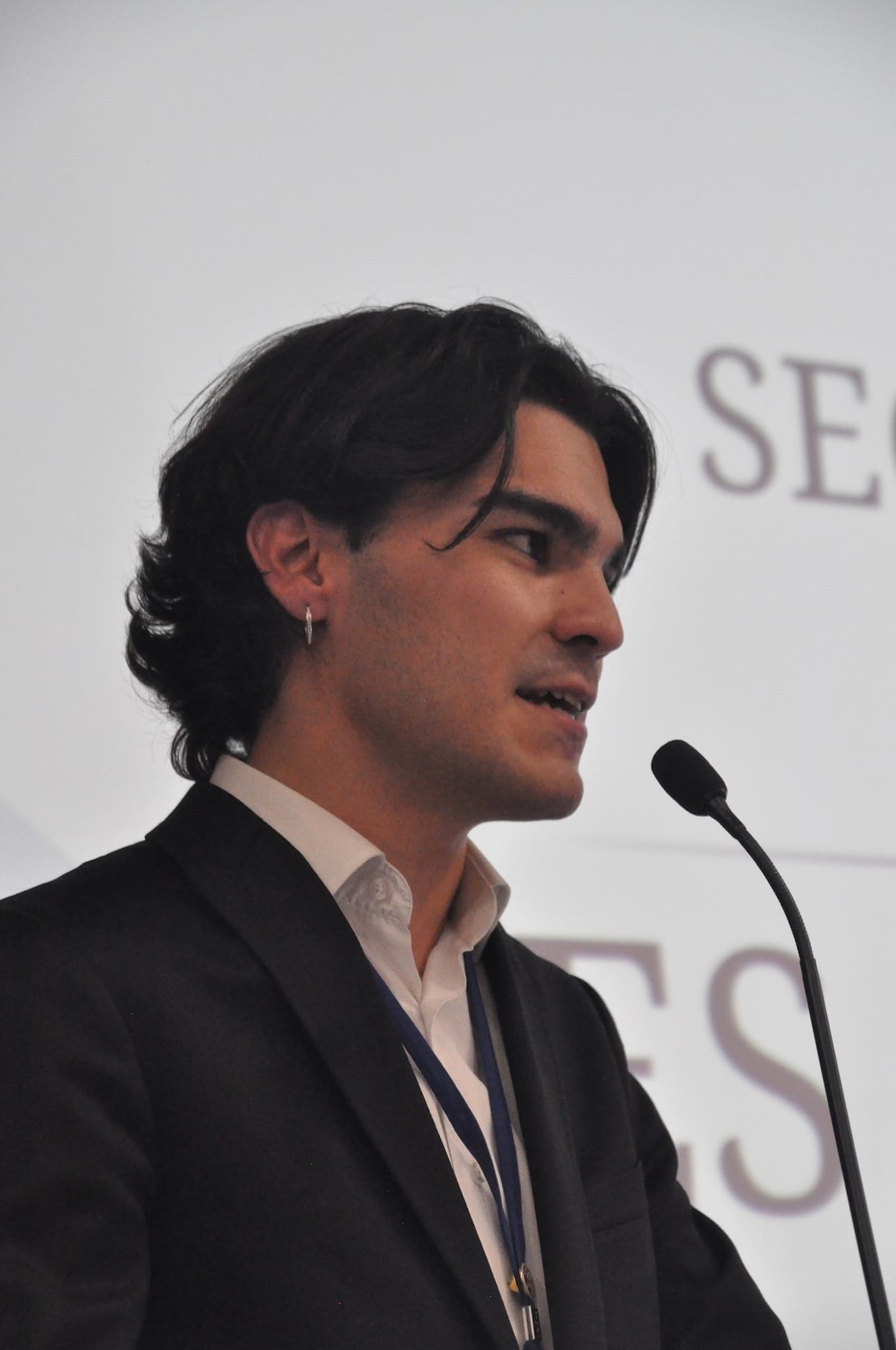 Ein Porträtfoto von Enes, wie er in ein Mikrofon spricht.