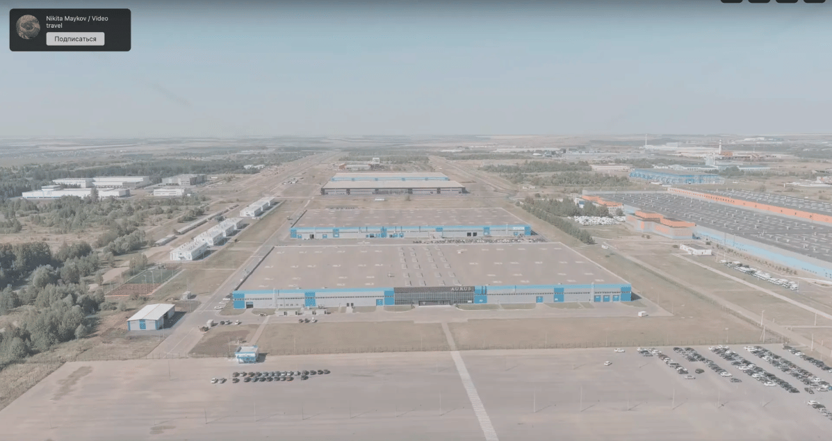 Man sieht ein weites Areal, auf dem in der Ferne Autos und Gebäude zu sehen sind.