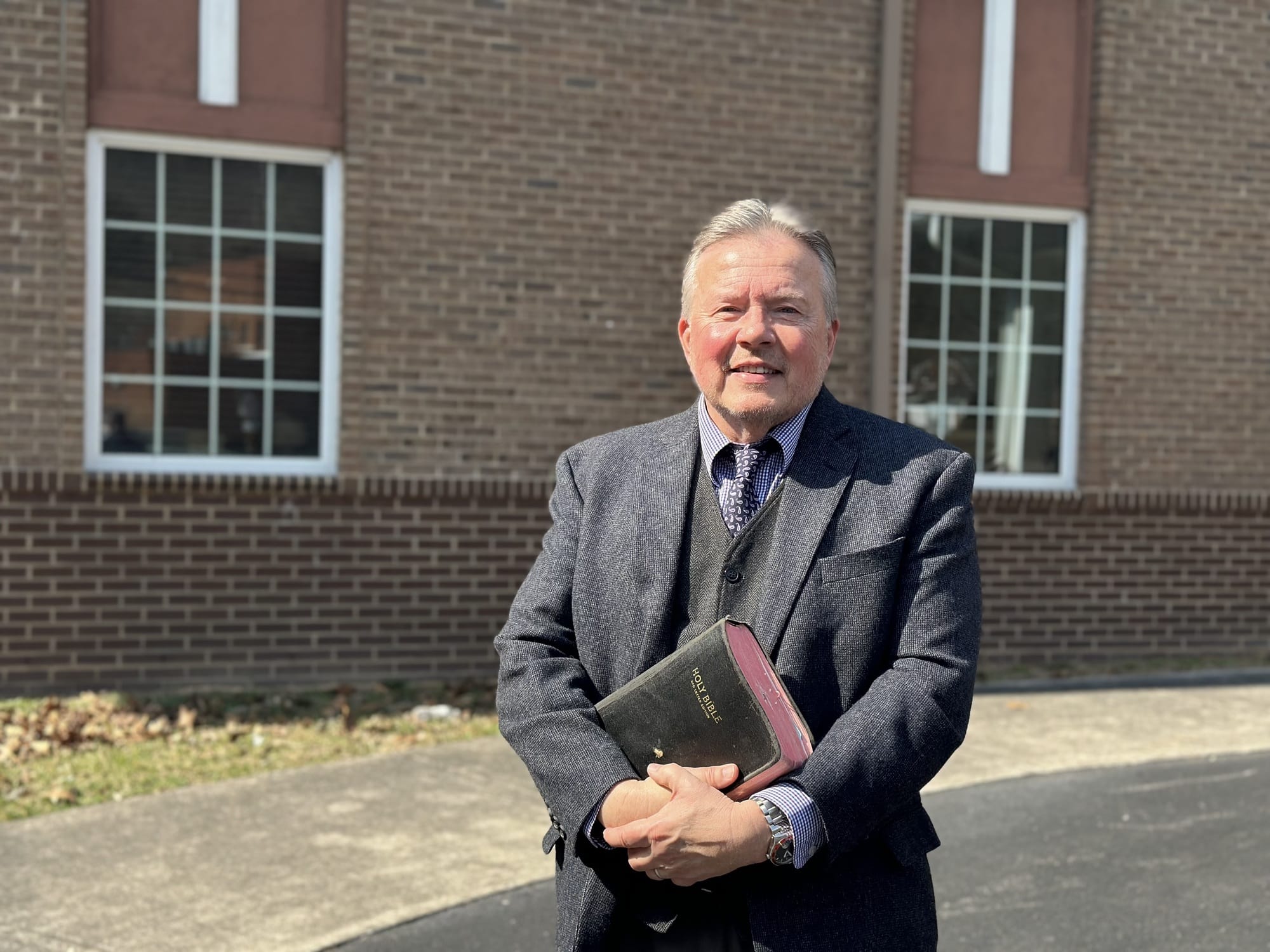 Ein Mann hat eine Bibel in der Hand und steht vor einer Kirche.