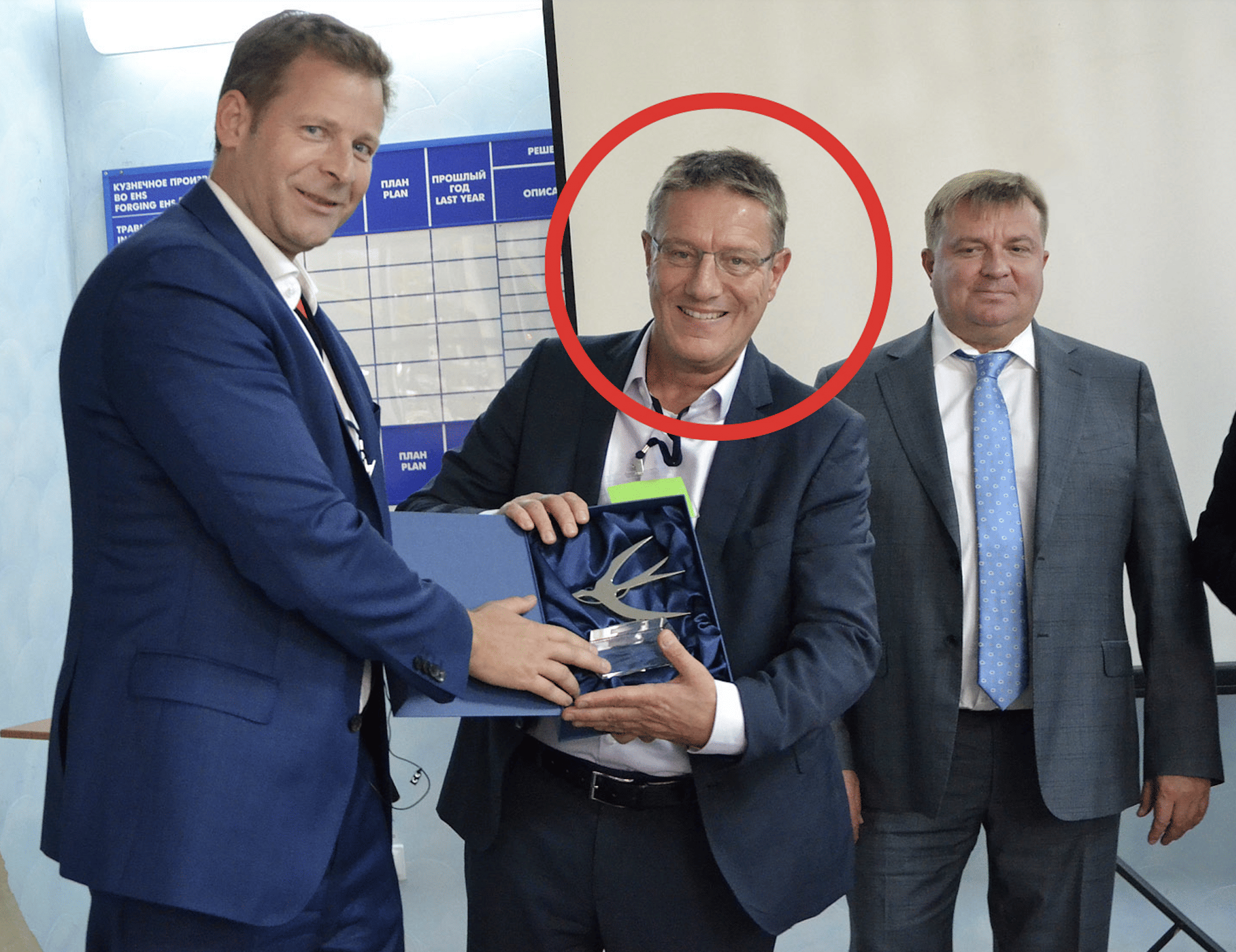 Man sieht drei Männer, einer davon hält ein Firmenlogo in der Hand.