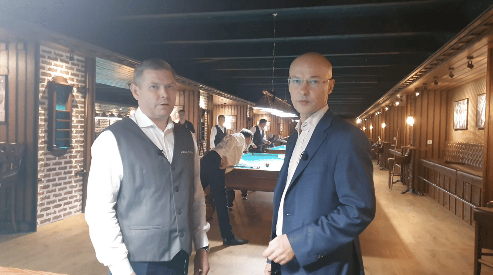 Man sieht zwei Männer, im Hintergrund spielen Menschen Billard.