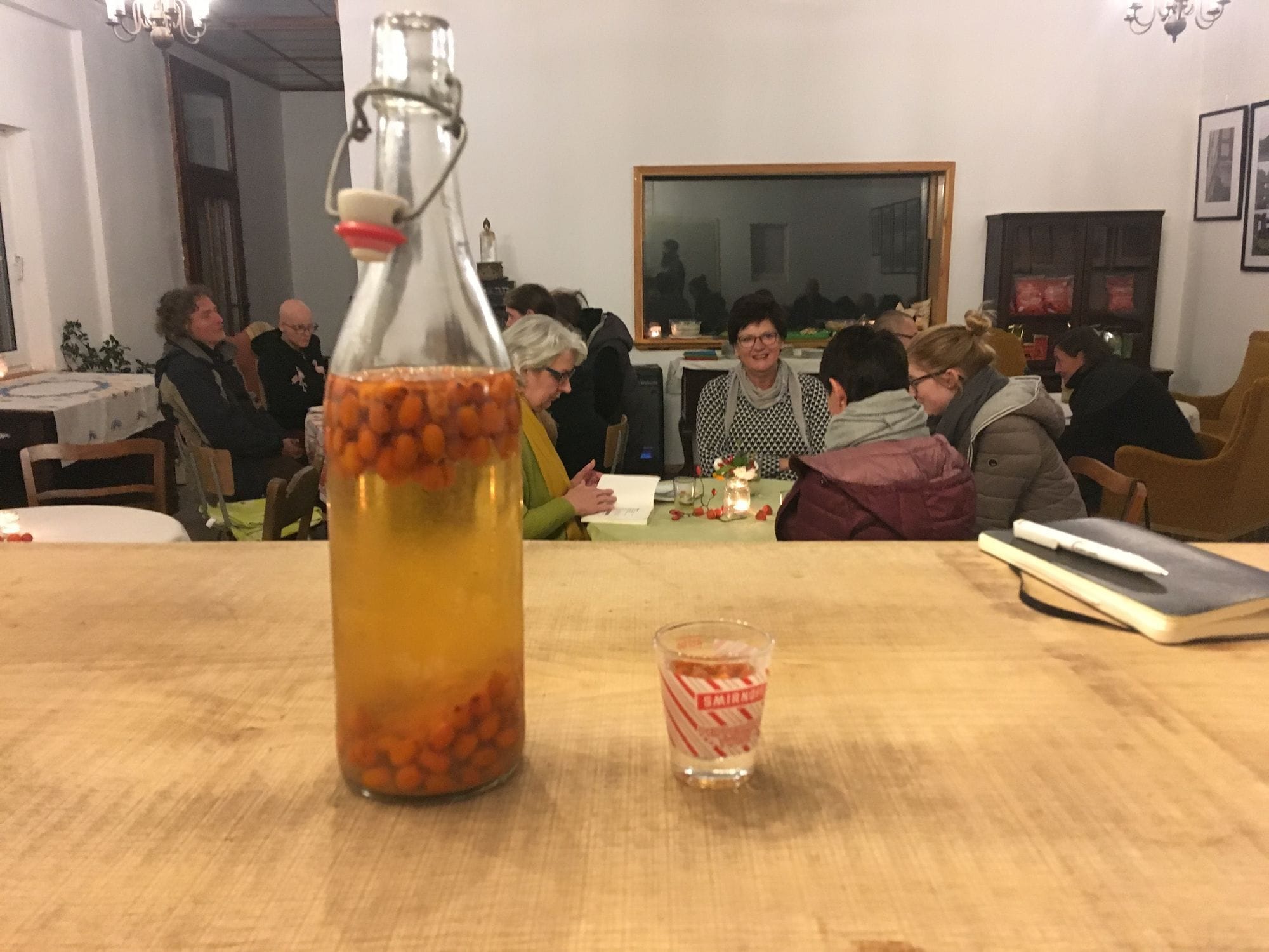 Sanddorn-Schnapsflasche im Vordergrund, sprechende Gruppe im Hintergrund
