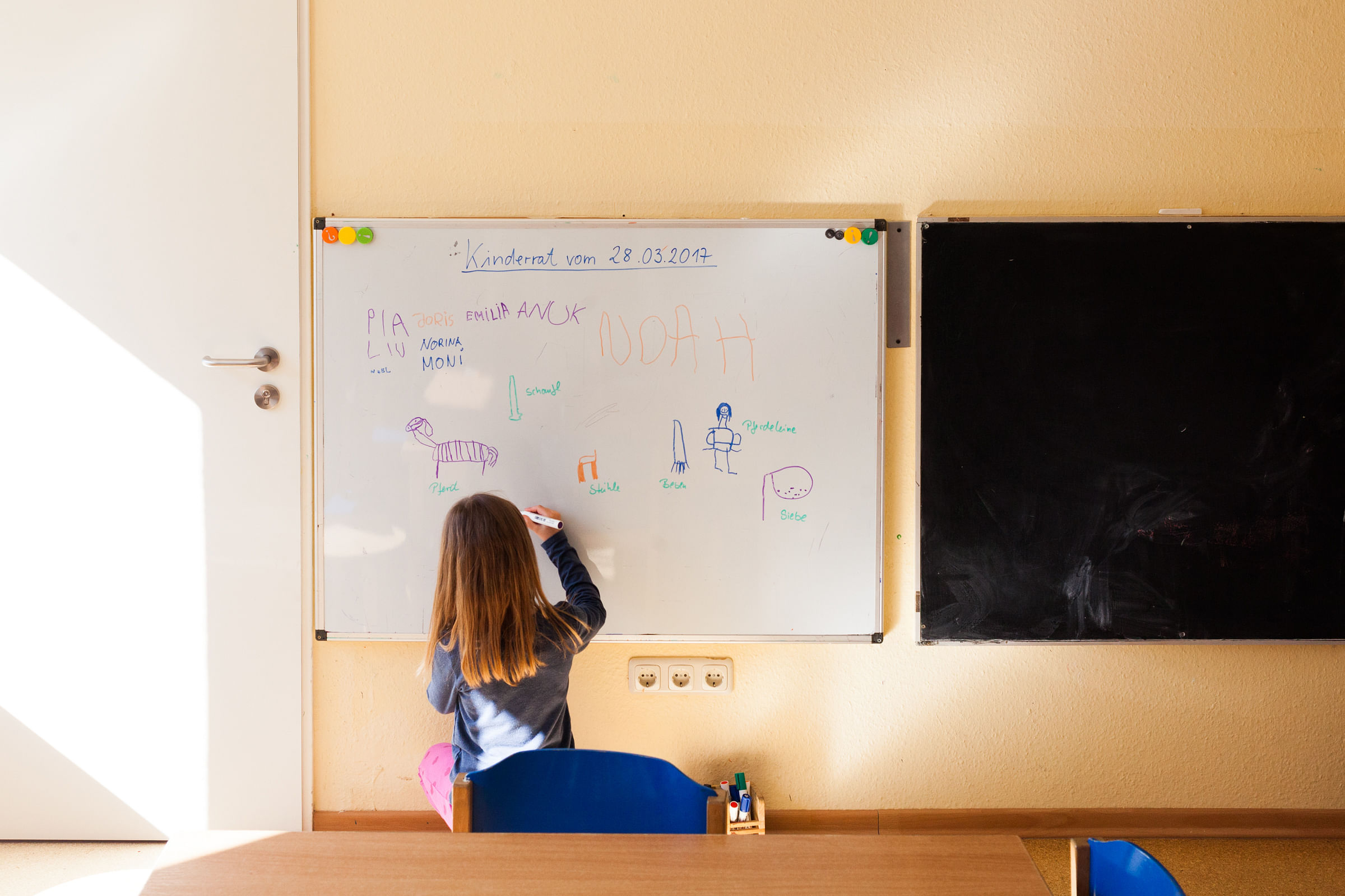 Welche Spielsachen brauchen wir für den Sommer? Anuk malt ihre Idee auf ein Whiteboard.