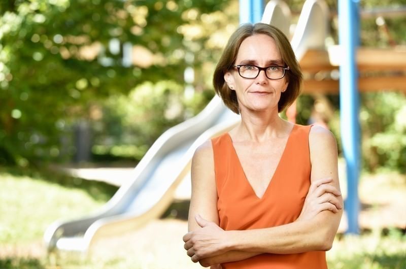 Hier sieht man eine Frau, die in eine orangenen shirt in die Kamera lächelt.