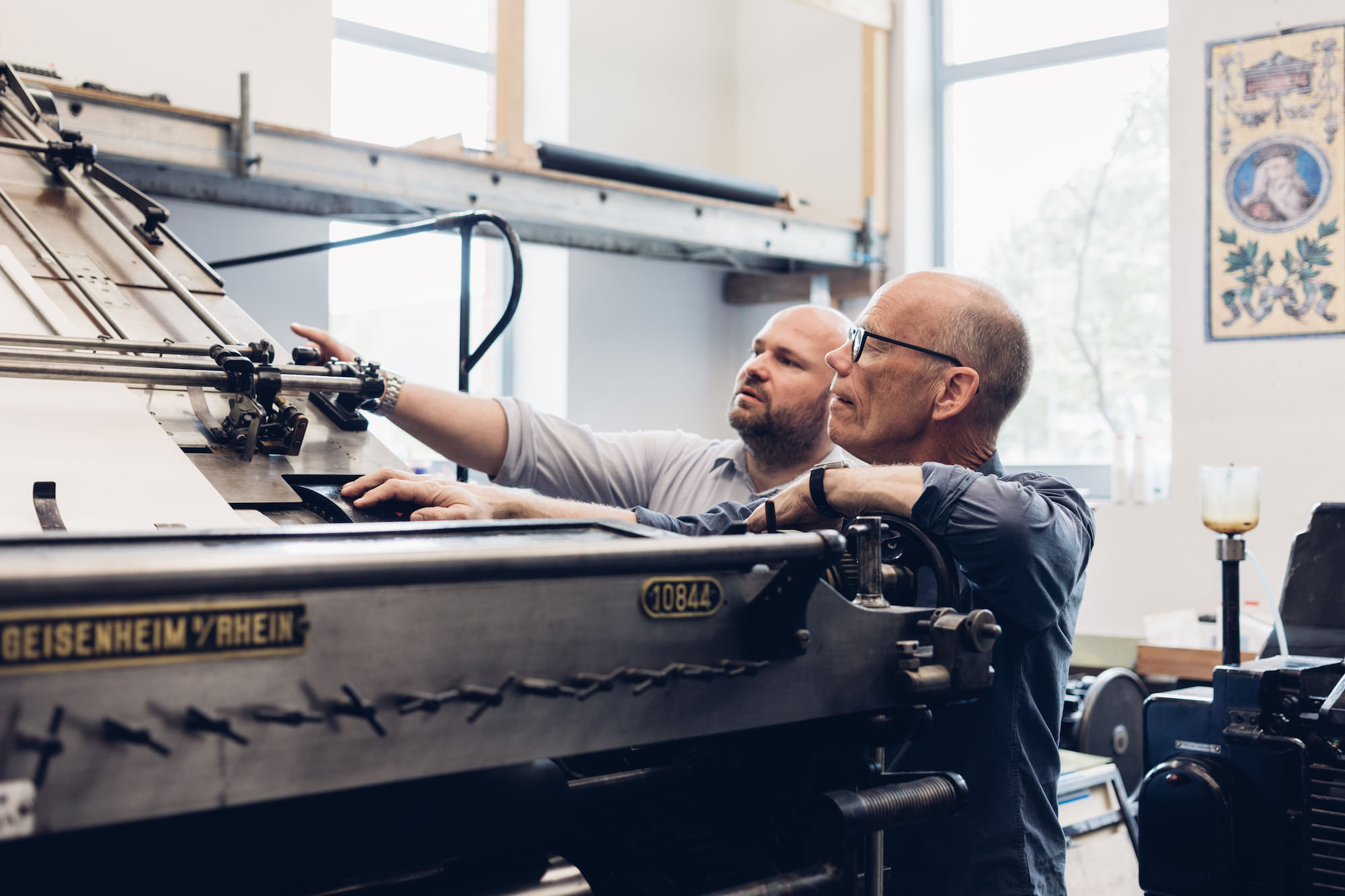 Das Papier gleitet zwischen dem Zylinder und dem Schlitten ein und wird bedruckt. Vorn sind ungefähr ein Dutzend Walzen, wo Farbe aufgetragen und verrieben wird. Mit im Bild: der Retter und Restaurator der Druckmaschine, Daniel Klotz.