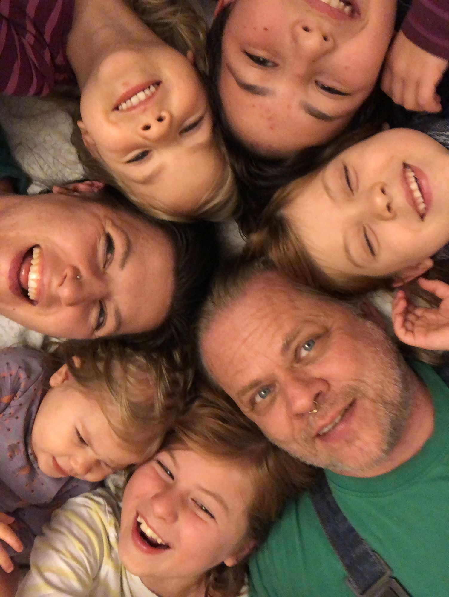 Man sieht ein Mann und eine Frau und dazu fünf Kinder, alle lachen und haben die Köpfe eng zusammengesteckt.