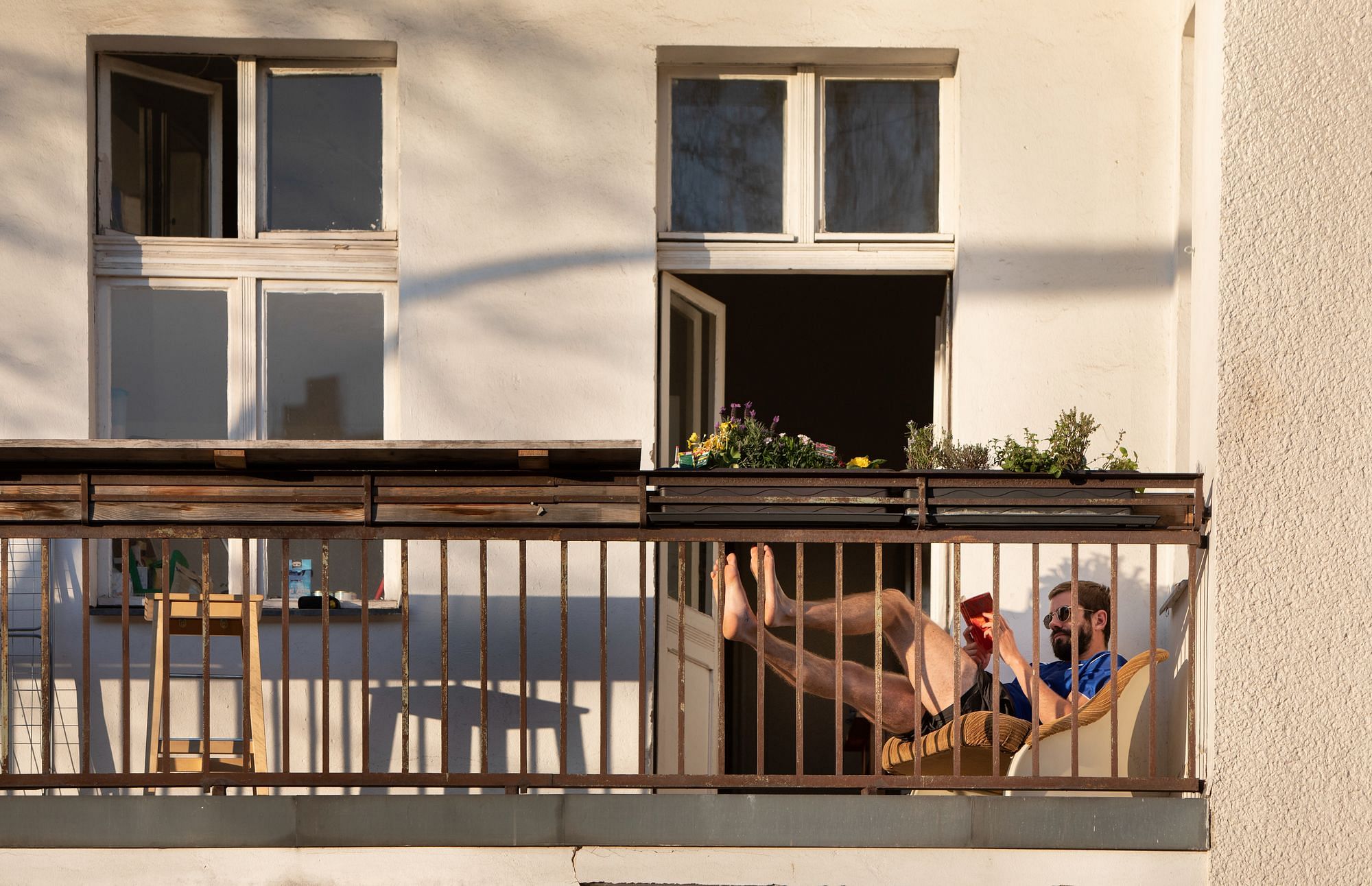 Ein Mensch sitzt auf seiner Liege auf dem Balkon und liest ein Buch und trägt eine Sonnenbrille.
