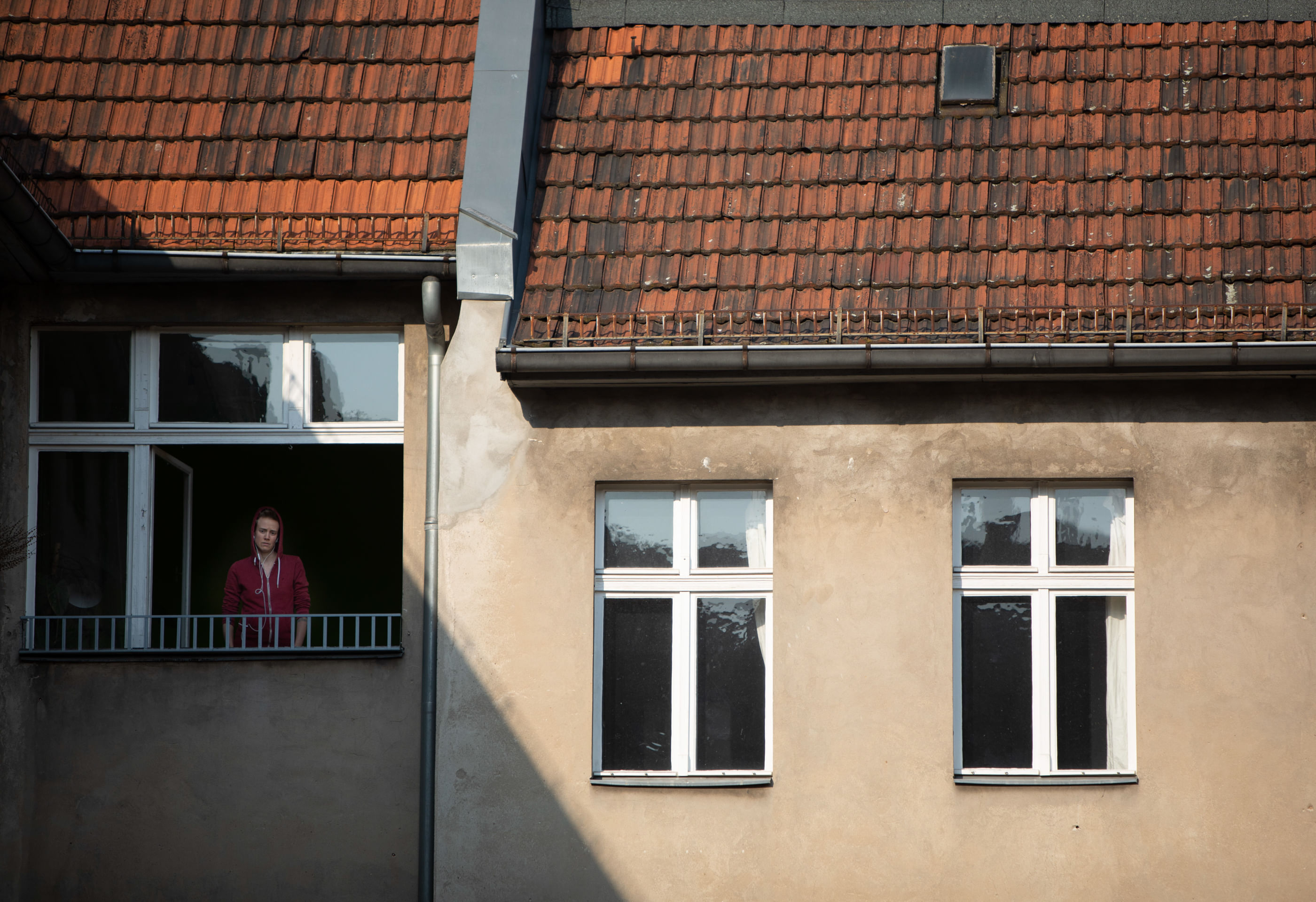 Wir sehen einen Menschen hinter seinem geöffneten Fenster – ein Dach wirft einen Schatten über den Menschen.