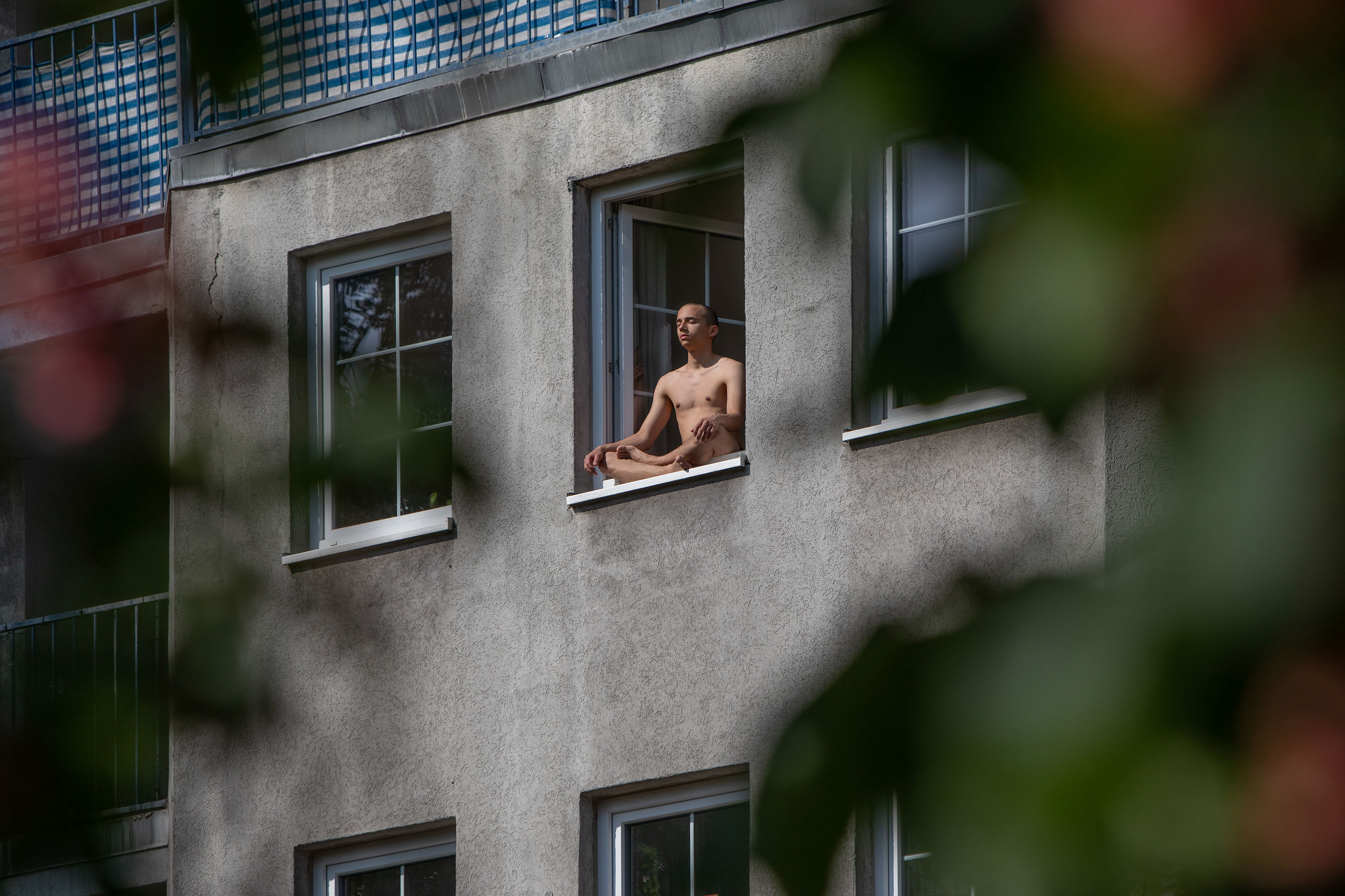 Ein Mann meditiert auf dem Fenstersims mit geschlossenen Augen und im Schneidersitz.