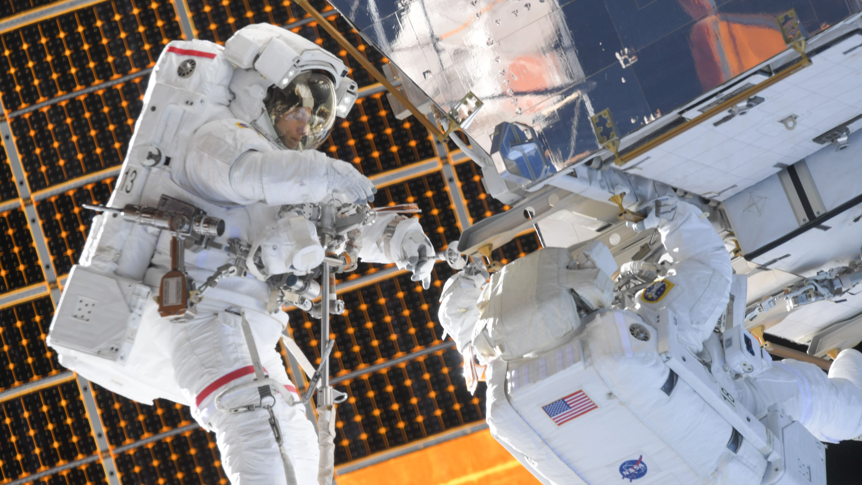 Wir sehen zwei Astronautinnen, die an einem größeren Bauteil etwas reparieren.