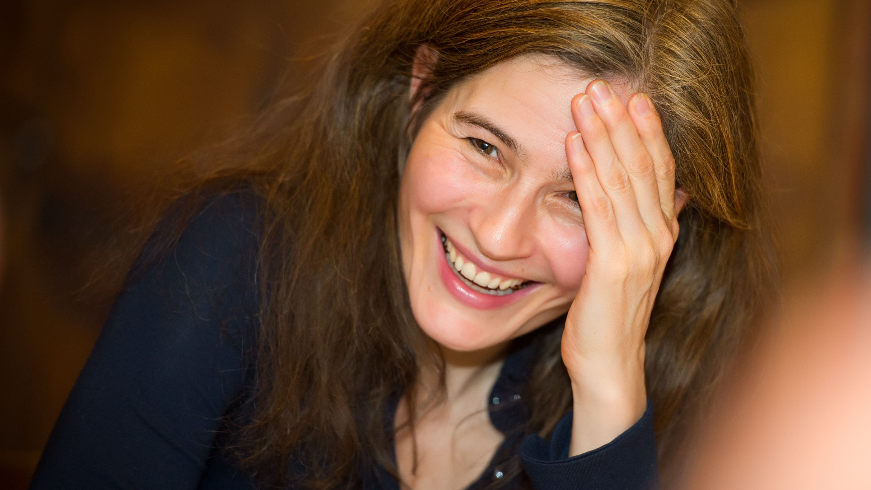 Wir sehen die Philosophine Natalie Knapp: Sie lacht und stützt ihren Kopf mit der linken Hand ab. 