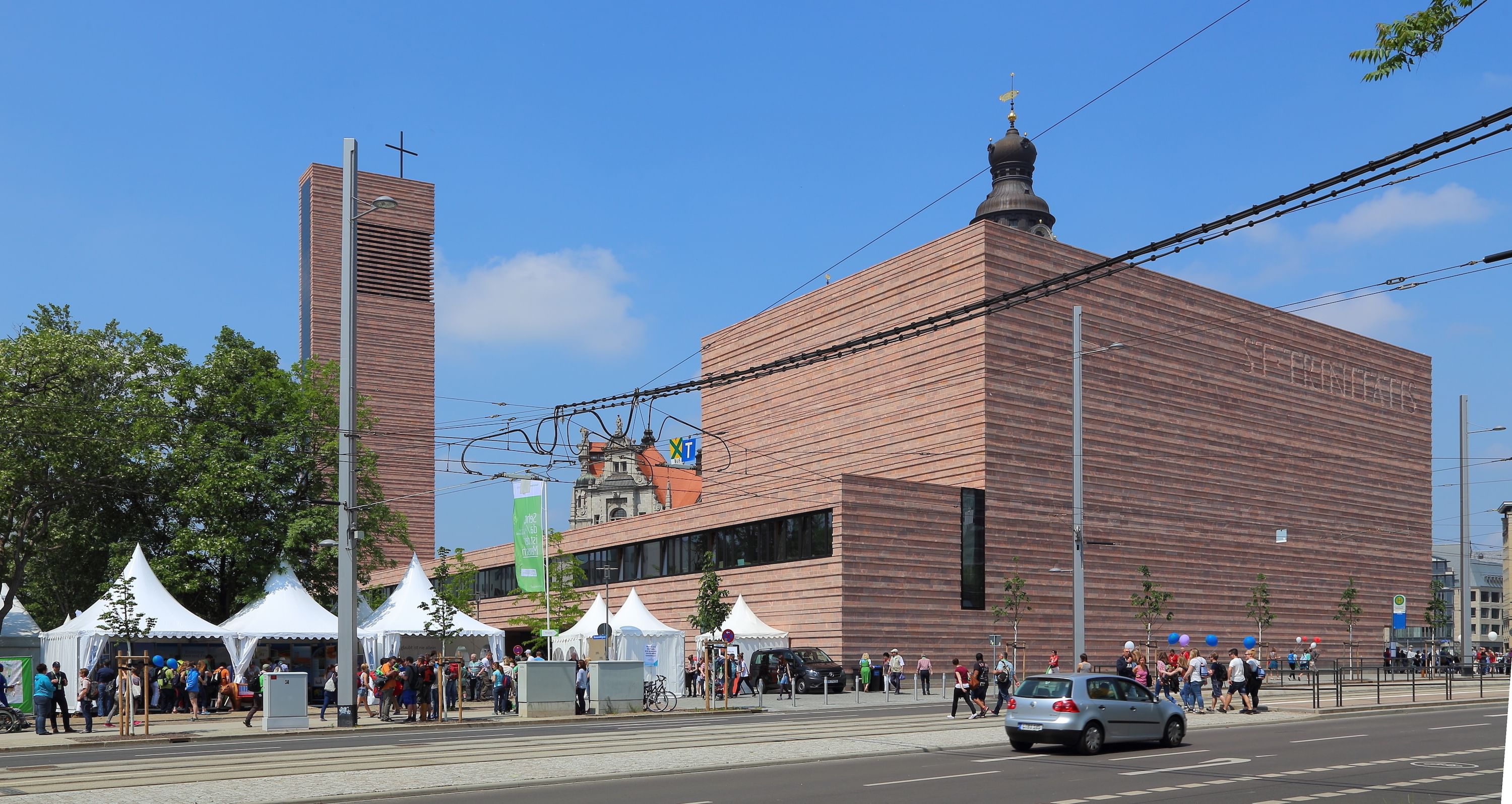 Wir sehen ein sehr strammes, quadratisches Gebäude, klare Kanten, braun in der Farbe und ein Kirchenturm. Es sieht auf den ersten Blick nicht aus, wie eine Kirche.