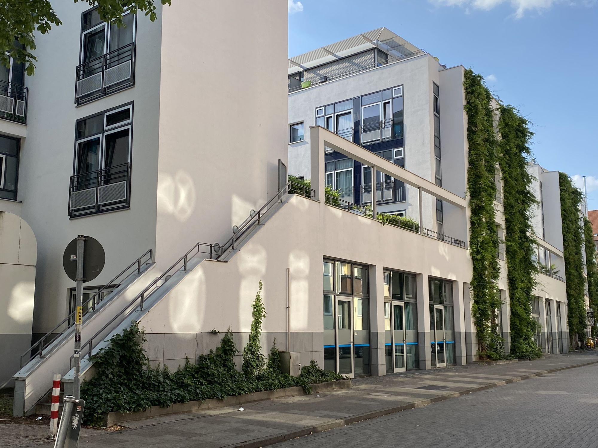 Ein helles, modernes Gebäude, schräg anfotografiert – an den Wänden entlang nach oben ragt grüne Bepflanzung
