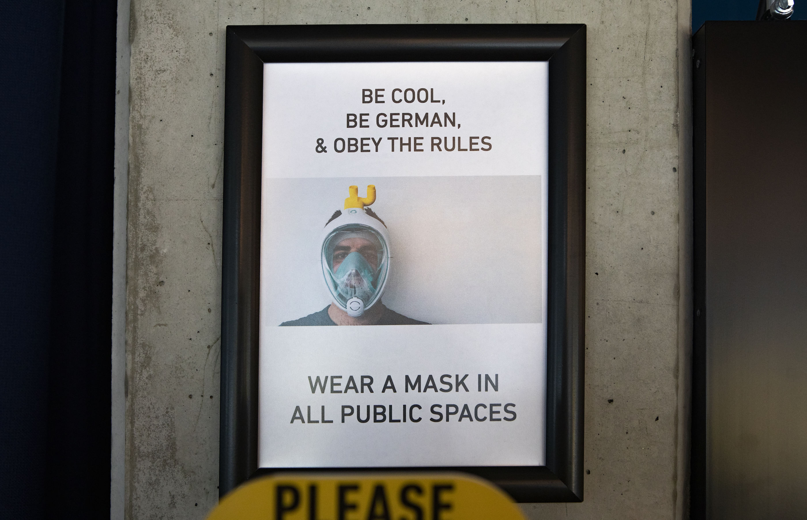 Wir sehen ein Plakat, eingerahmt mit folgendem Spruch: Be cool, be German, wear a Mask in all public spaces