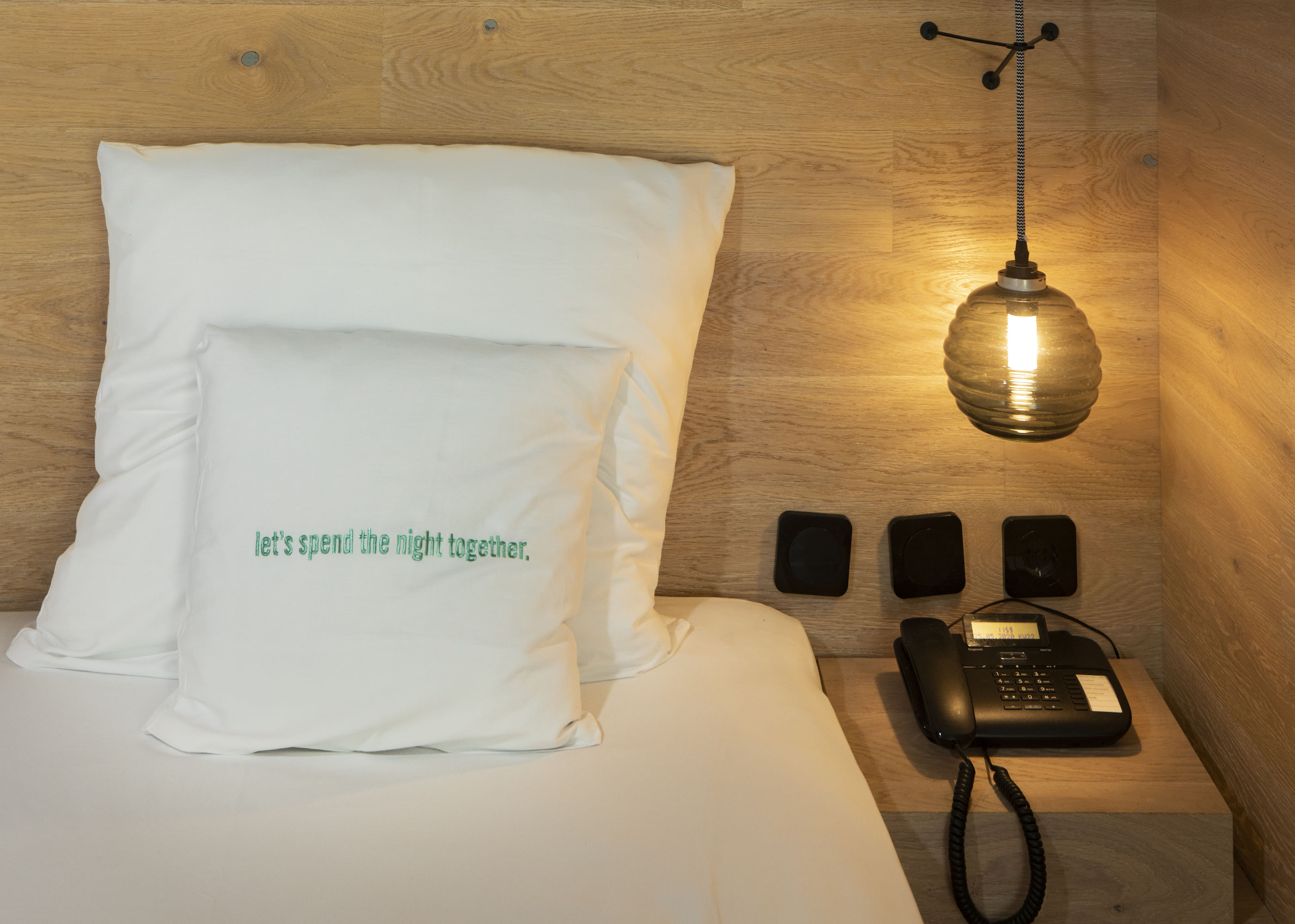 Wir sehen das obere Ende eines Bettes und angelehnt ein weißes Kissen mit der Aufschrift: Lets spend the night together