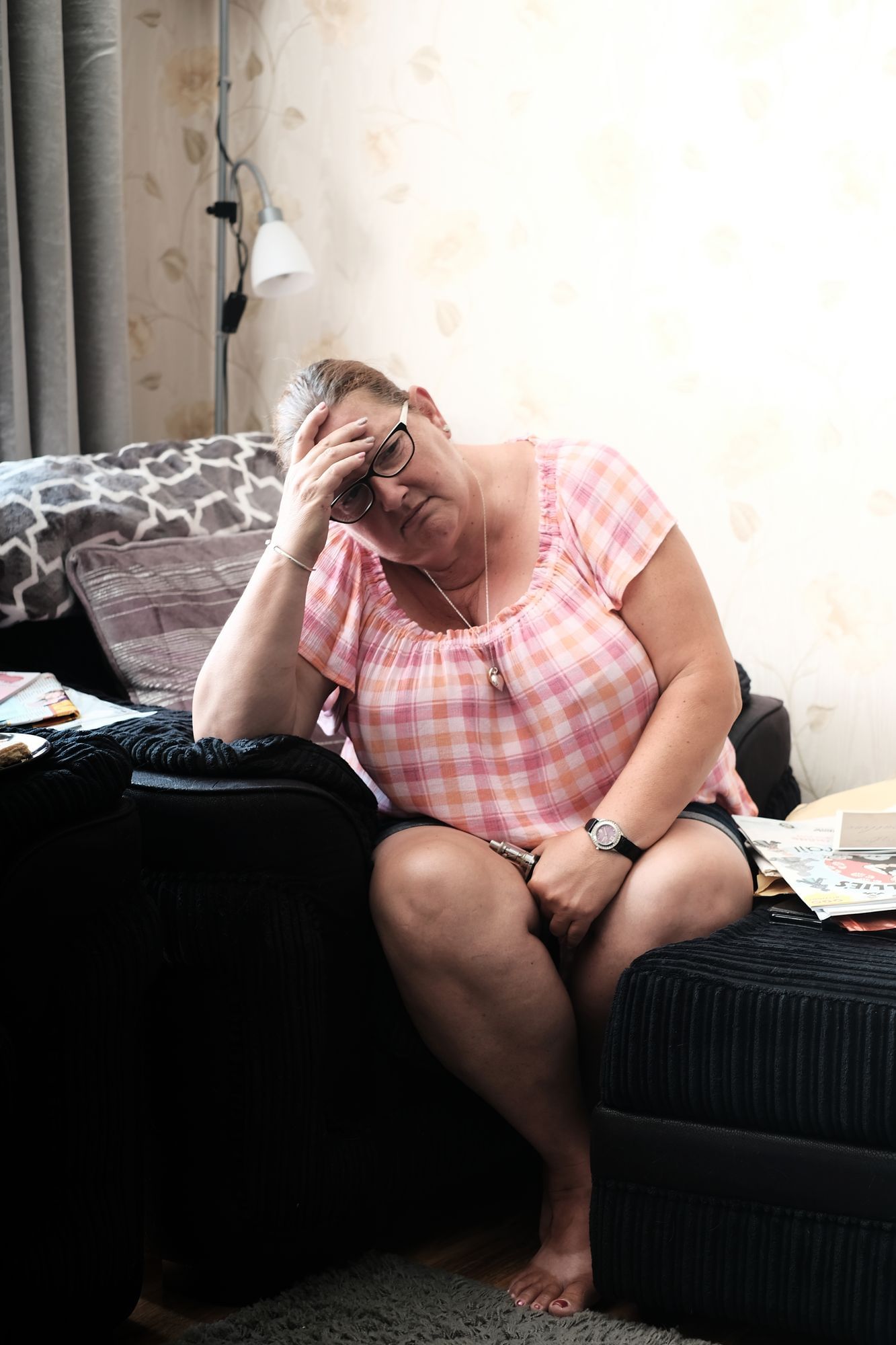 Die Frau Shelly Grigg sitzt auf ihrem Sofa, stützt sich mit der Hand ab und hat einen nach unten gerichteten traurigen Blick.