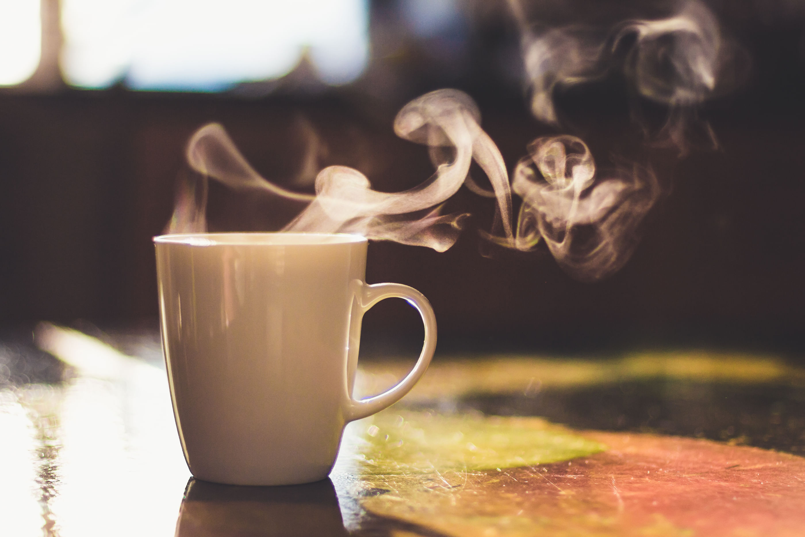 Wir sehen eine weiße Kaffeetasse, aus der Dampf steigt.