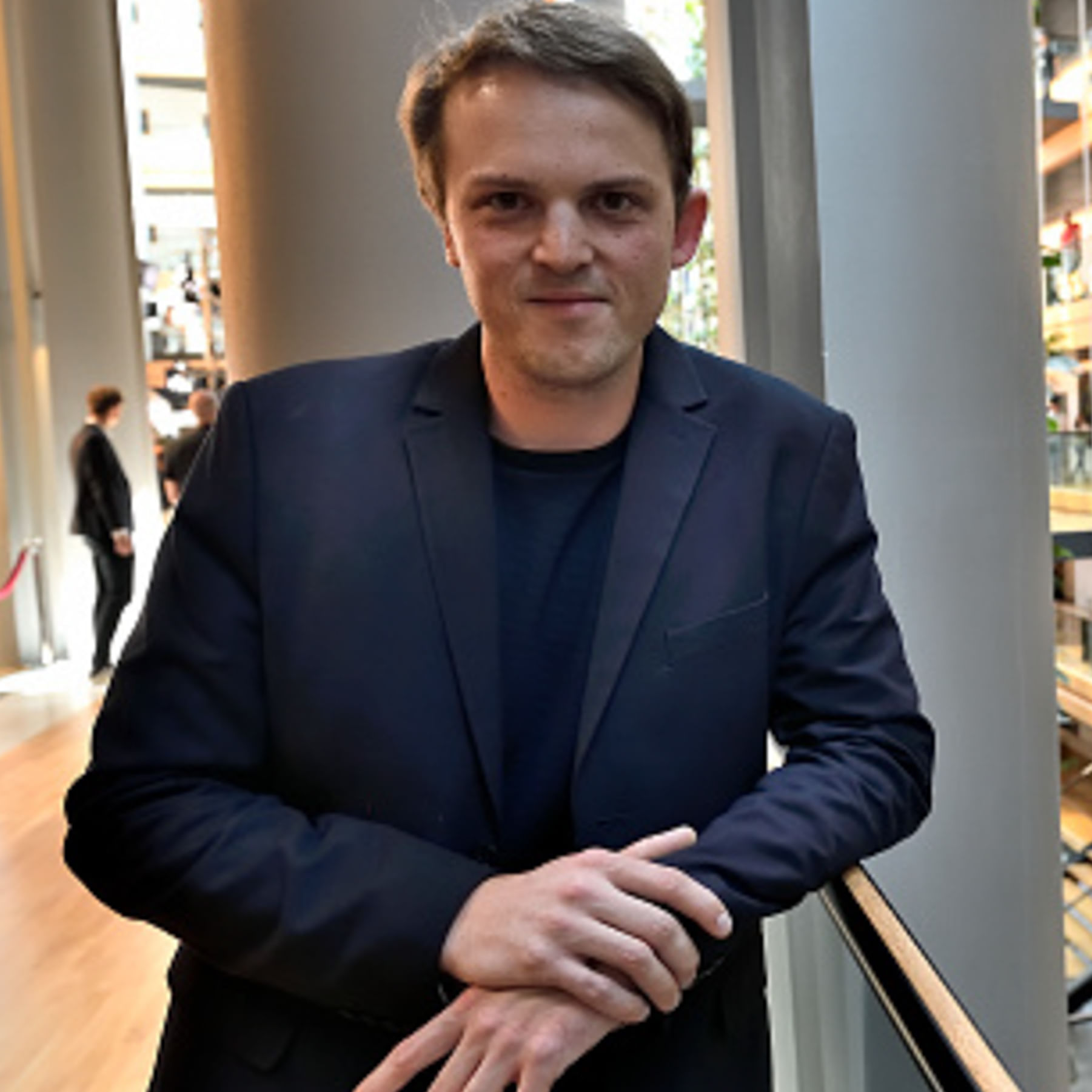 Porträt von Erik Marquardt, einem jungen Mann im schwarzen Anzug, der sichgegen eine Brüstung lehnt