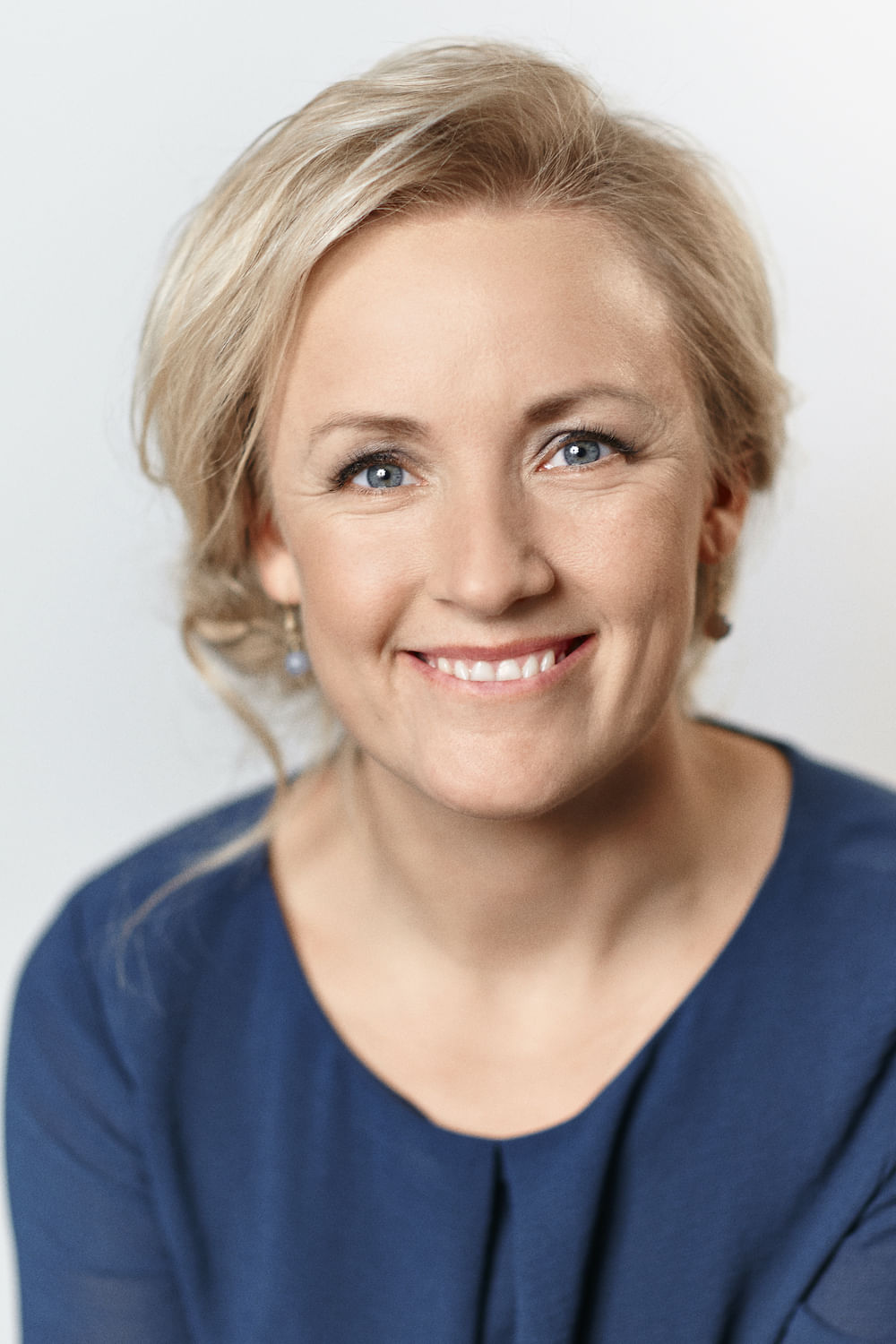 Wir sehen die Autorin, die in die Kamera lächelt. Sie hat ein freundliches, offenes Gesicht, blonde Haare und blaue Augen.