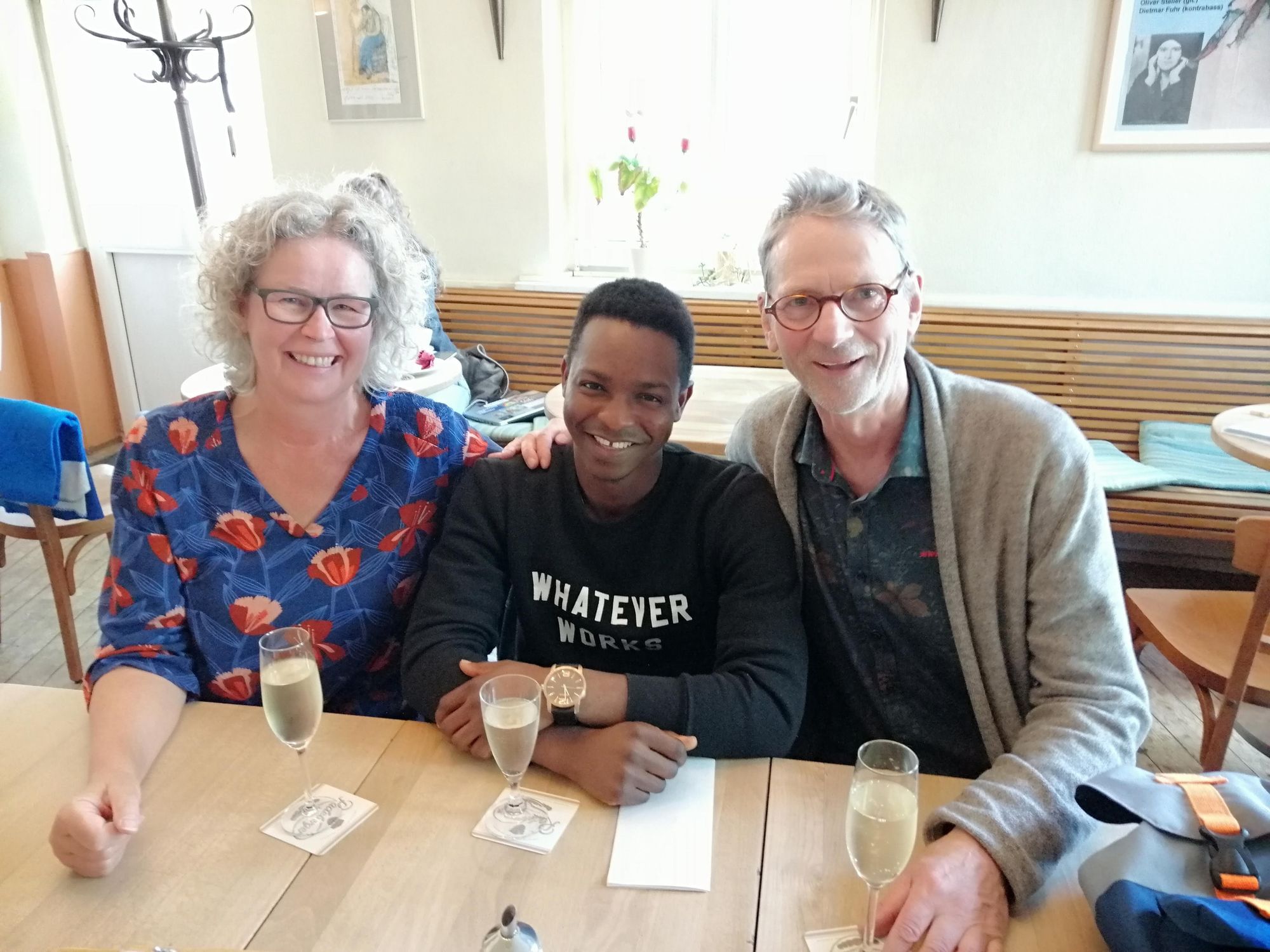 Ulla und ihr Mann sitzen mit Moudje in der Mitte zusammen am Tisch mit einem Glas Sekt. Das Bild wurde am Tag der offiziellen Adoption aufgenommen.