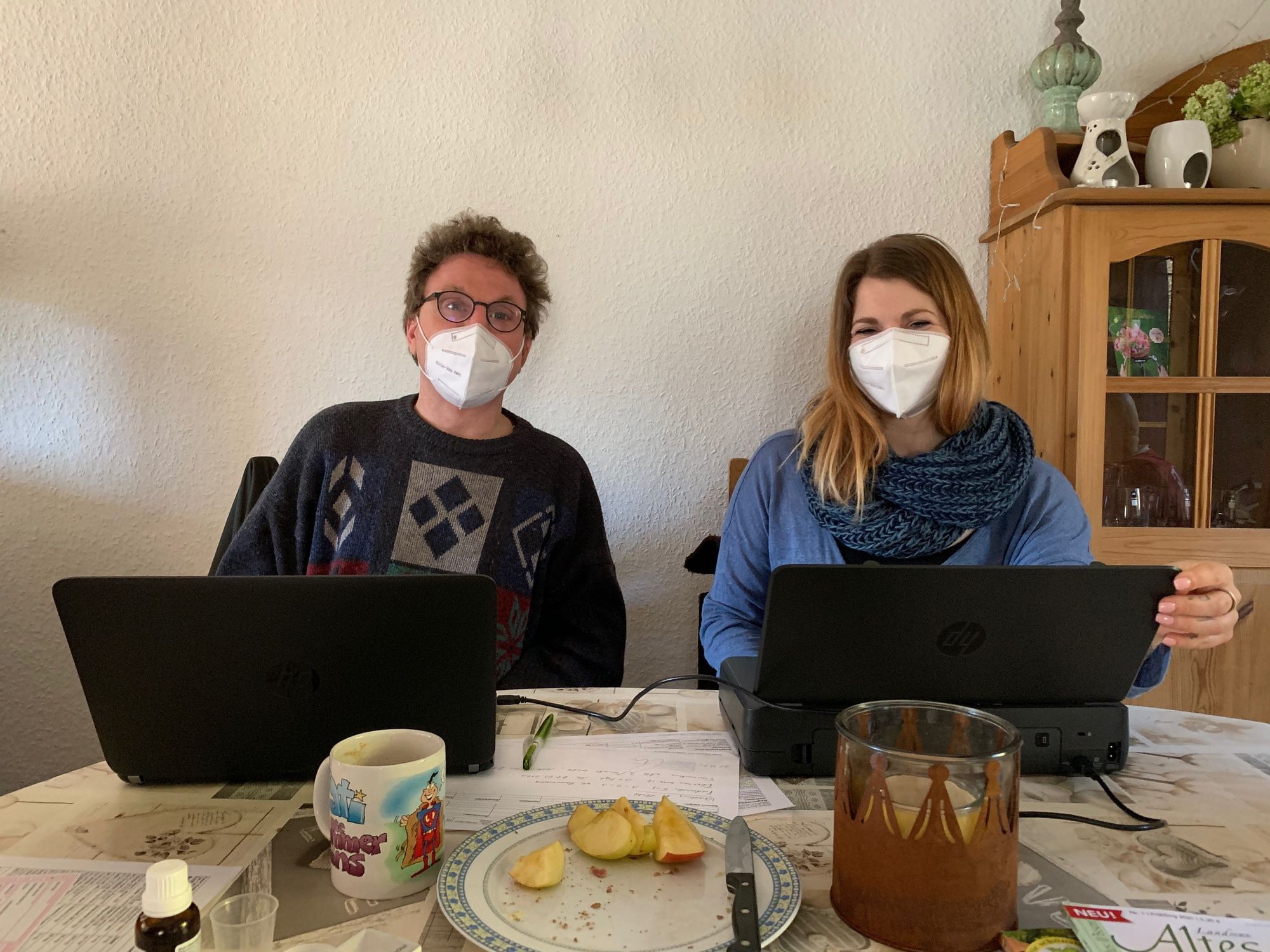 Das Bild zeigt Volker Barth und Julia Bäumker am Küchentisch eines Patienten. Barth hat einen aufgeklappten Laptop vor sich, Beumker einen mobilen Drucker.