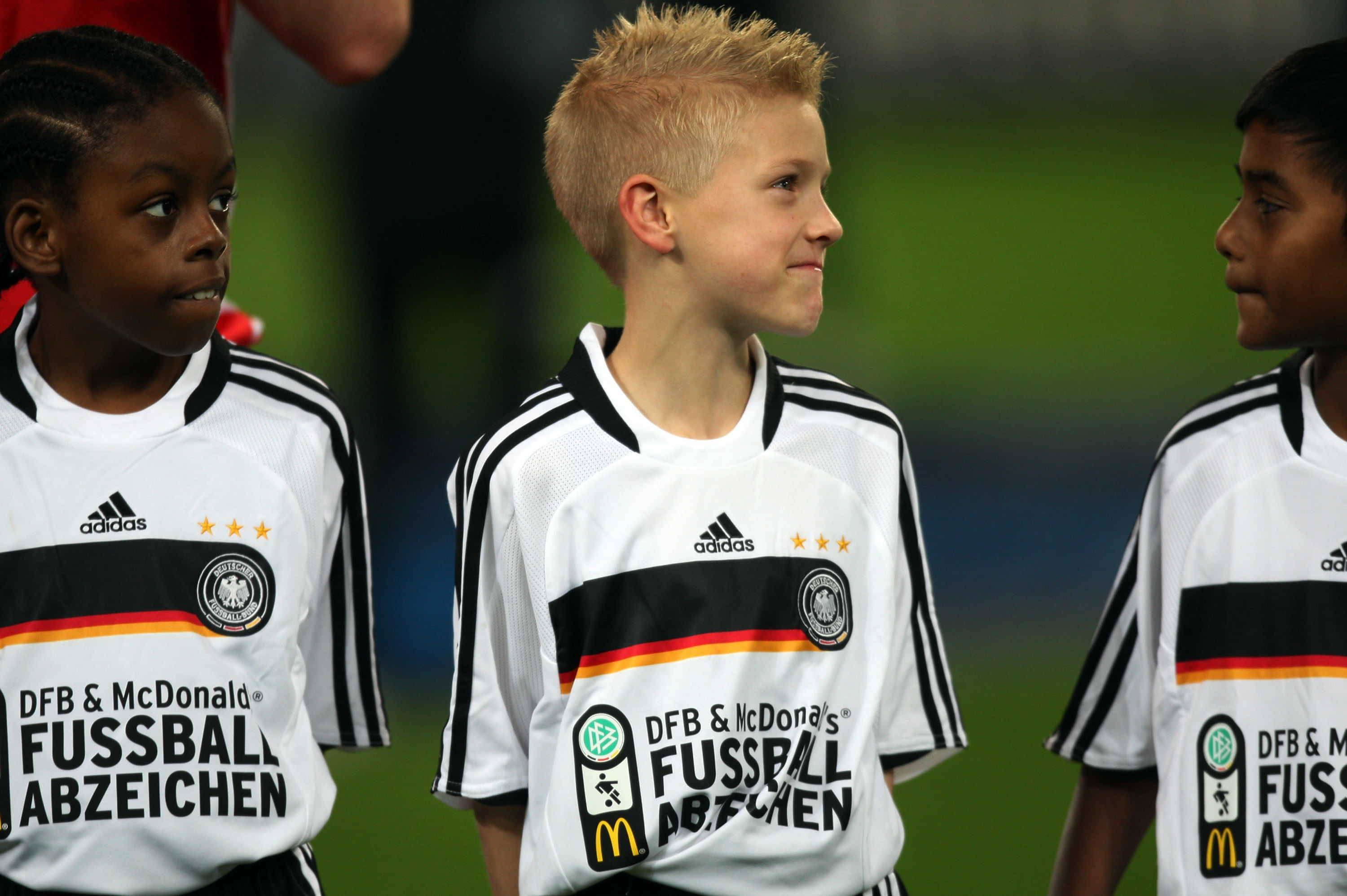 Drei Jungen in offiziellen Deutschland Trikots, alle neugierig und freudig, einer breit grinsend.