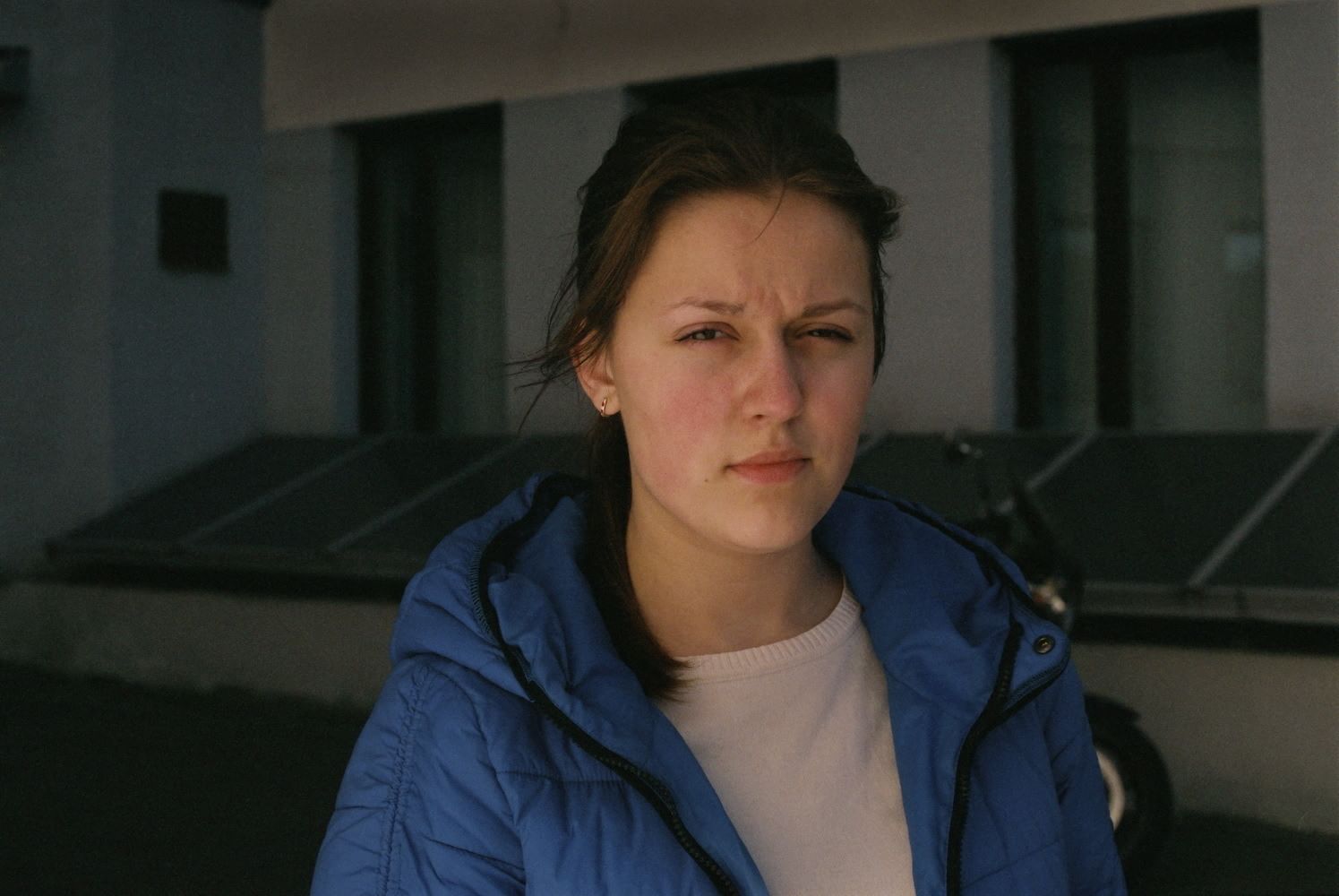 Eine kritisch beäugende junge Frau blick mit einem Auge in die Kamera, das andere ist geschlossen.