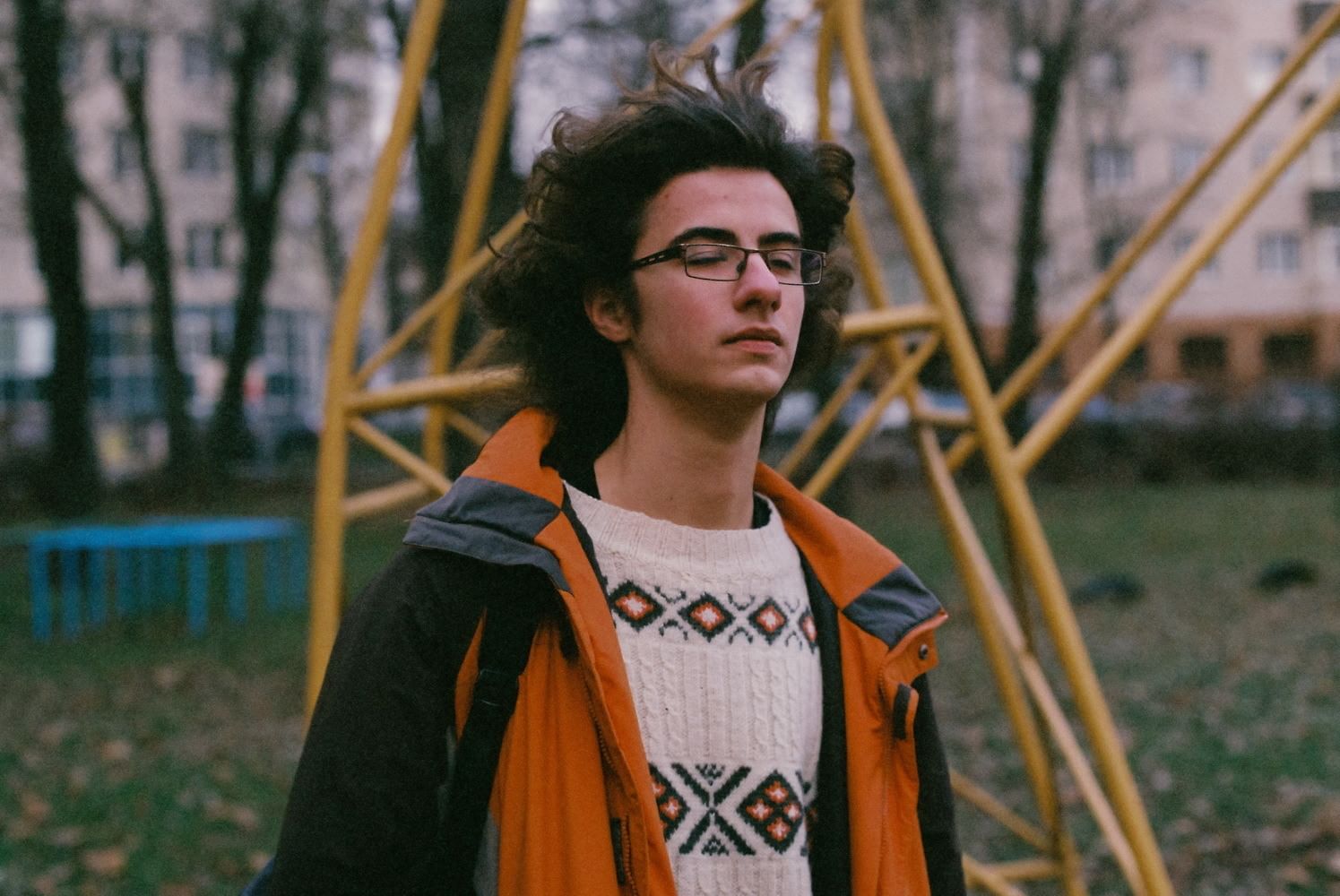 Ein junger Mann mit Brille und geschlossenen Augen scheint sich scheinbar nach vorne zu erheben. Seine Pose und Haltung deuten Mut und Hoffnung an. Im Hintergrund ist ein Klettergrüst einer Plattenbausiedlung zu sehen.