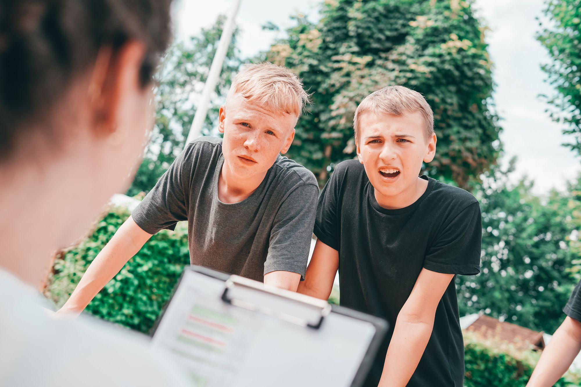 Zwei 14-jährigen Jungs stützen sich auf einem Tisch ab und guckcen eine Betreuerin fragend an. 
