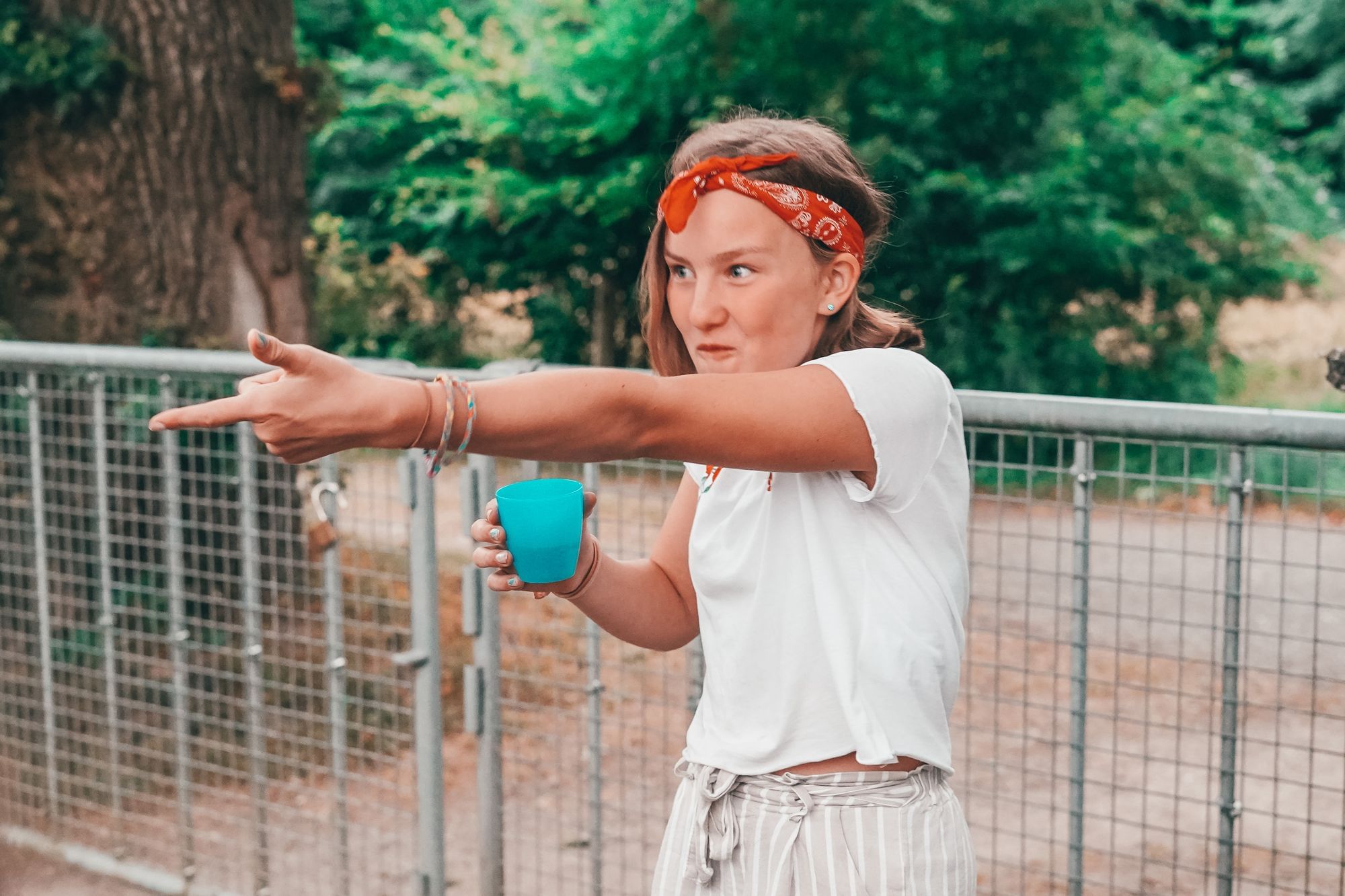 Ein Mädchen hält einen Becher in der Hand mit Wasser zum Gurgeln und zeigt mit der Hand in Richtung der anderen Kinder. 
