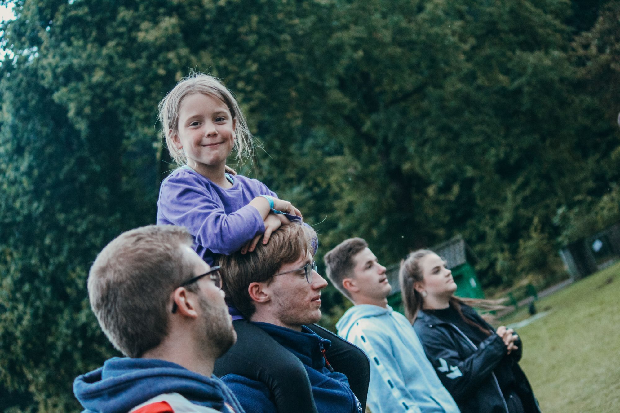 Ein siebenjähriges Mädchen sitzt auf den Schultern eines Betreuers und lächelt in die Kamera.