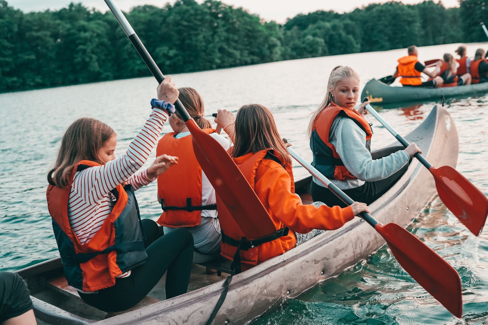 5 Mädchen sitzen im Kanu und paddeln über den See. 