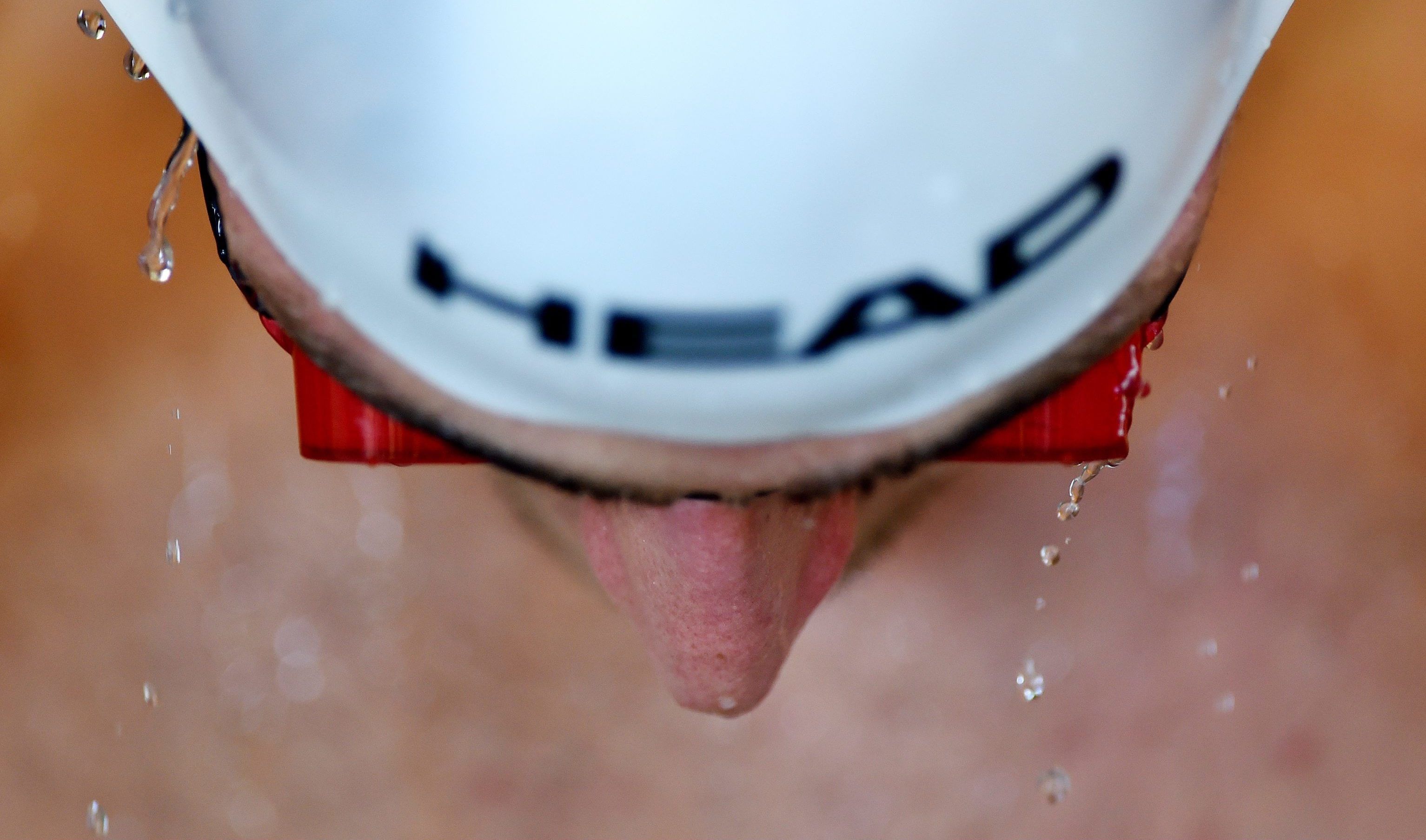 Wir sehen auf einen Menschen, der eine rote Schwimmbrille und eine weiße Kopfbedeckung trägt und nach unten sieht.