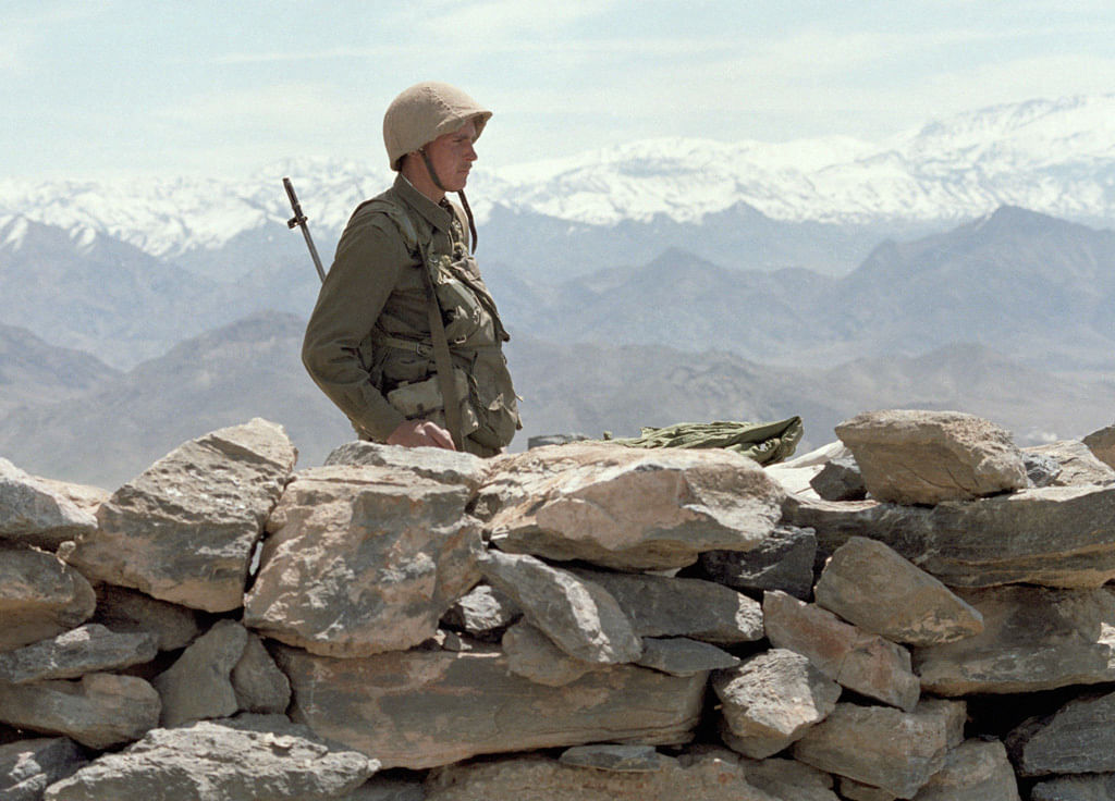 Ein Soldat steht mit Helm auf dem Kopf und Gewehr über der Schulter vor dem Hindukusch.