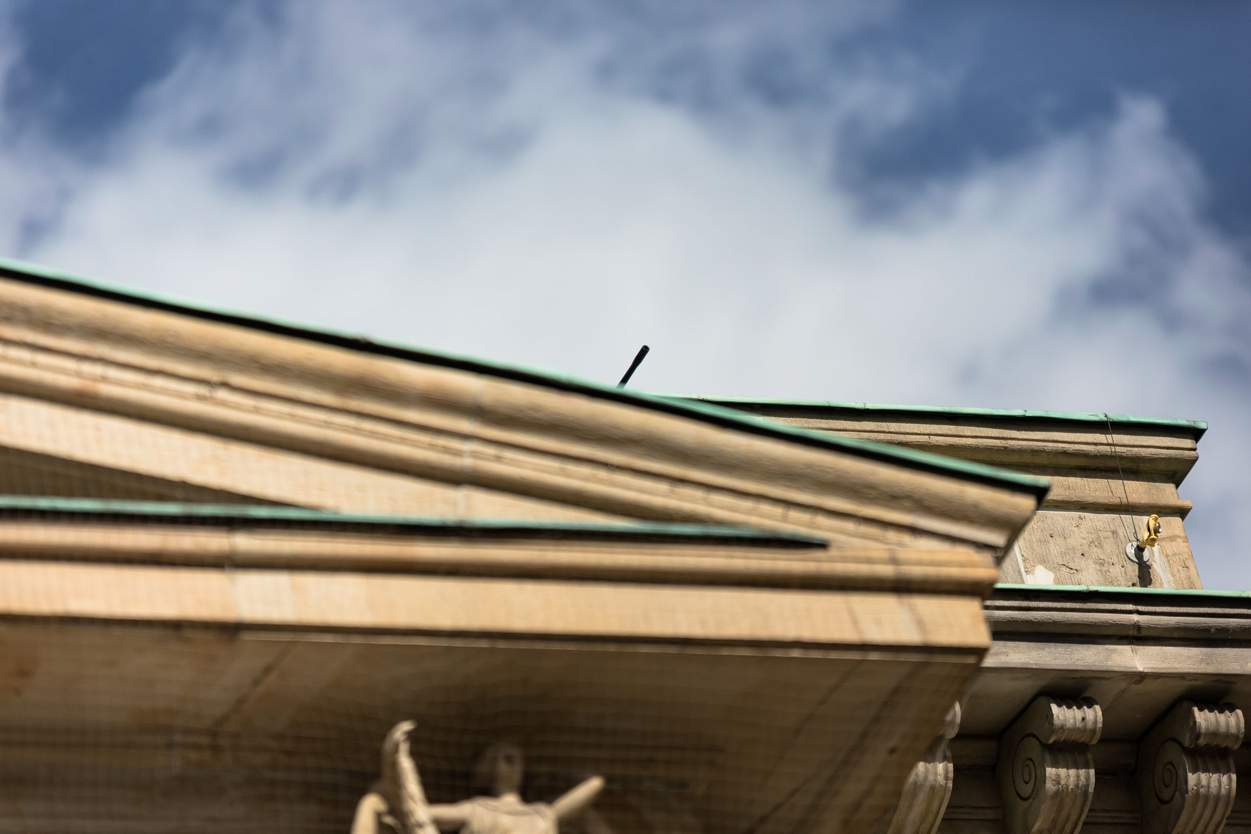 Der Porticus eines klassistischen Gebäudes, an dem sich ein runder schwarzer Gegenstand durch die Schärfe gegen Himmel abhebt.