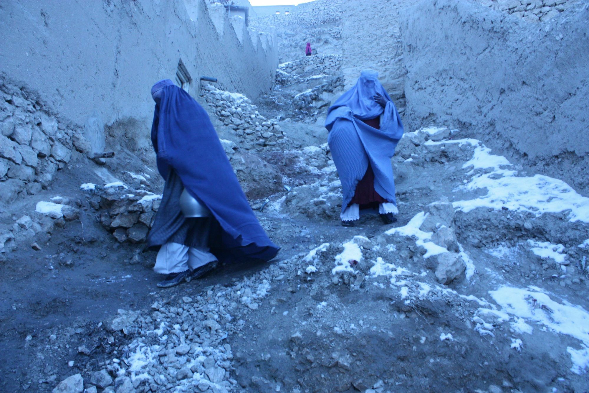 Zwei blaue Burka tragende Personen kommen eine bebaute Bergseite herab.