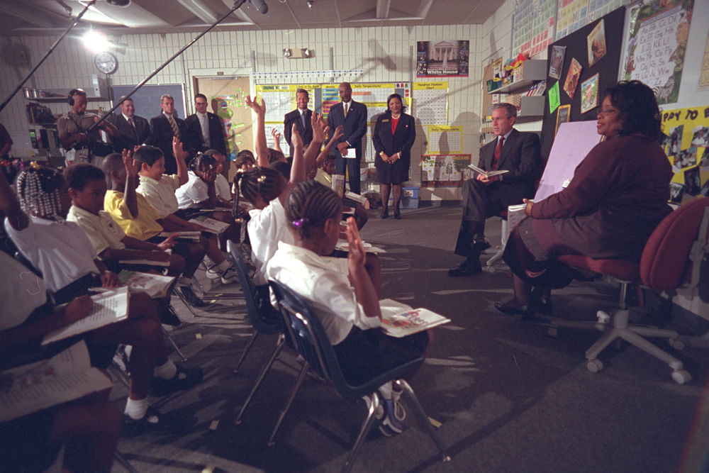 Eine US Grundschule, die Kinder im Alter zwischen 8 und 10 sitzen im Halbkreis mit Blick auf den  damals amtierenden Präsidenten George  W. Bush.