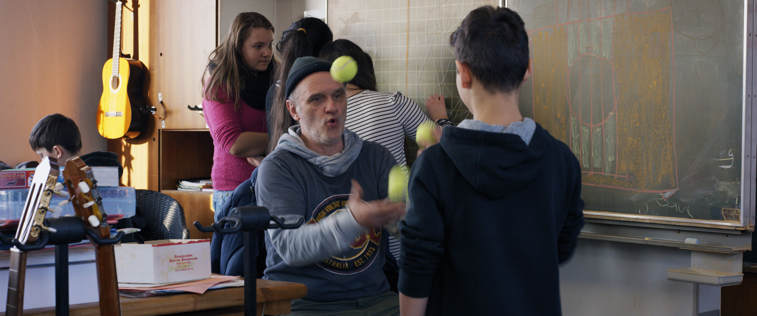 Herr Bachman jongliert vor einem Schüler mit drei Tennisbällen.